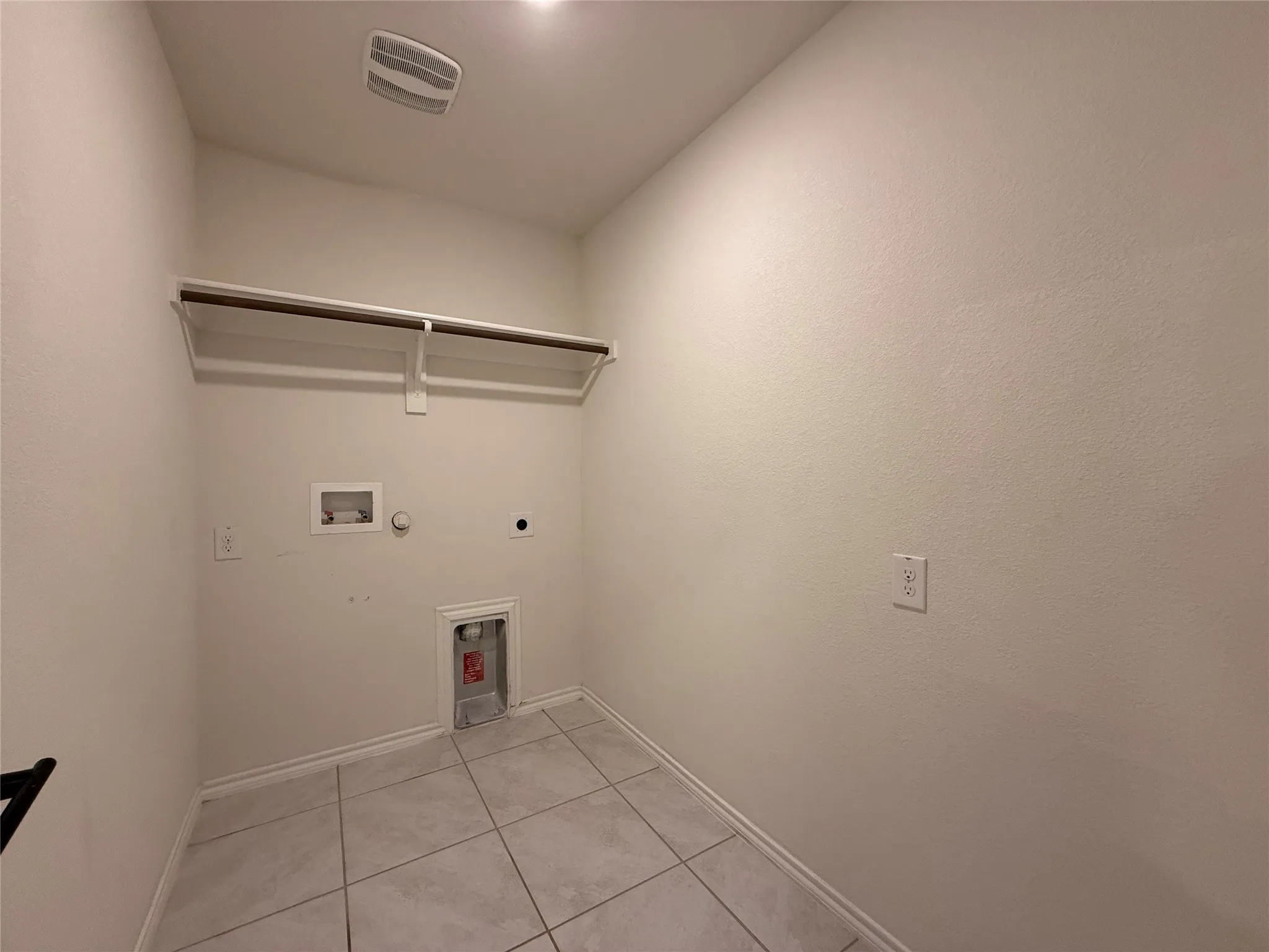 Dedicated laundry area featuring ceramic tile flooring, neutral wall tones, a built-in shelf with hanging rod, and essential appliance hookups