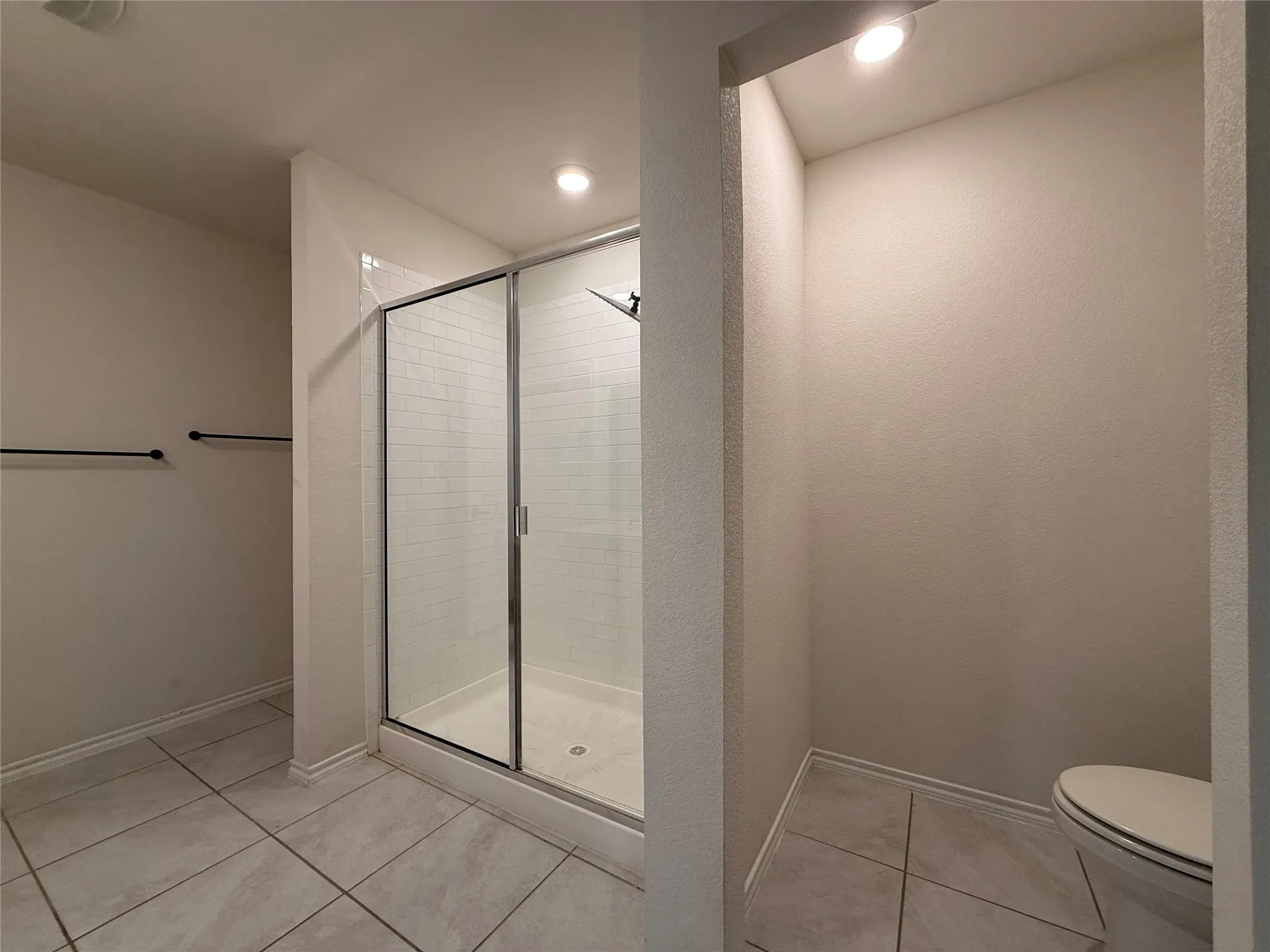 Bathroom featuring a glass-enclosed shower with subway tile surround, neutral-toned large format floor tiles, and recessed lighting