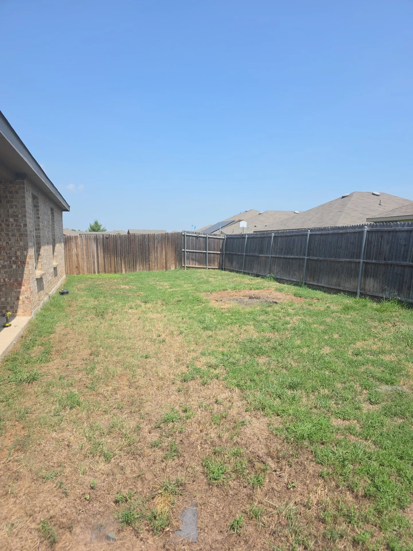 Expansive backyard space featuring a perimeter wood fence, partial brick exterior, and a large lawn area