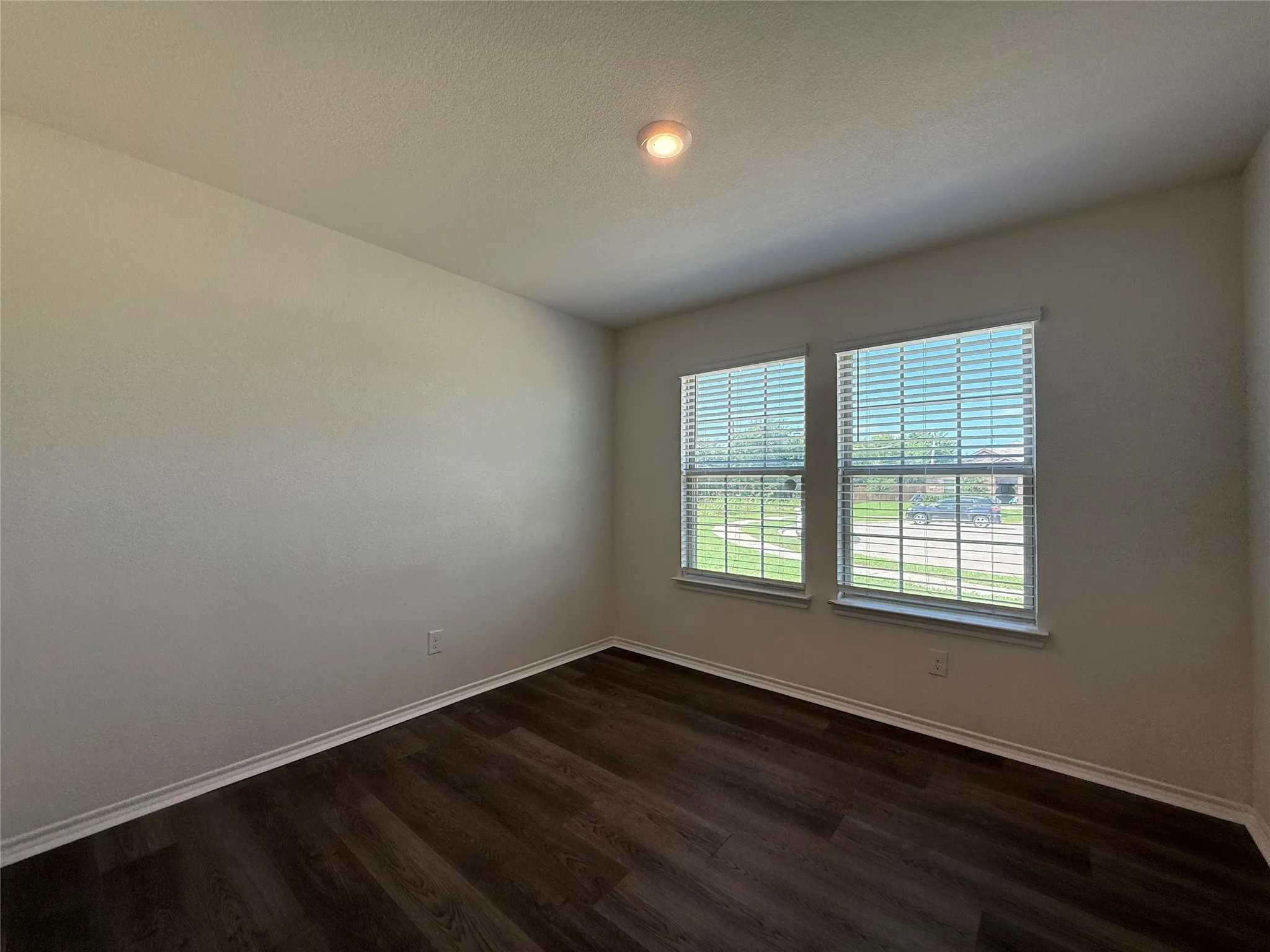 Room featuring wood-finish flooring, two large windows with blinds, light-toned wall paint, white trim, and a ceiling-mounted light fixture