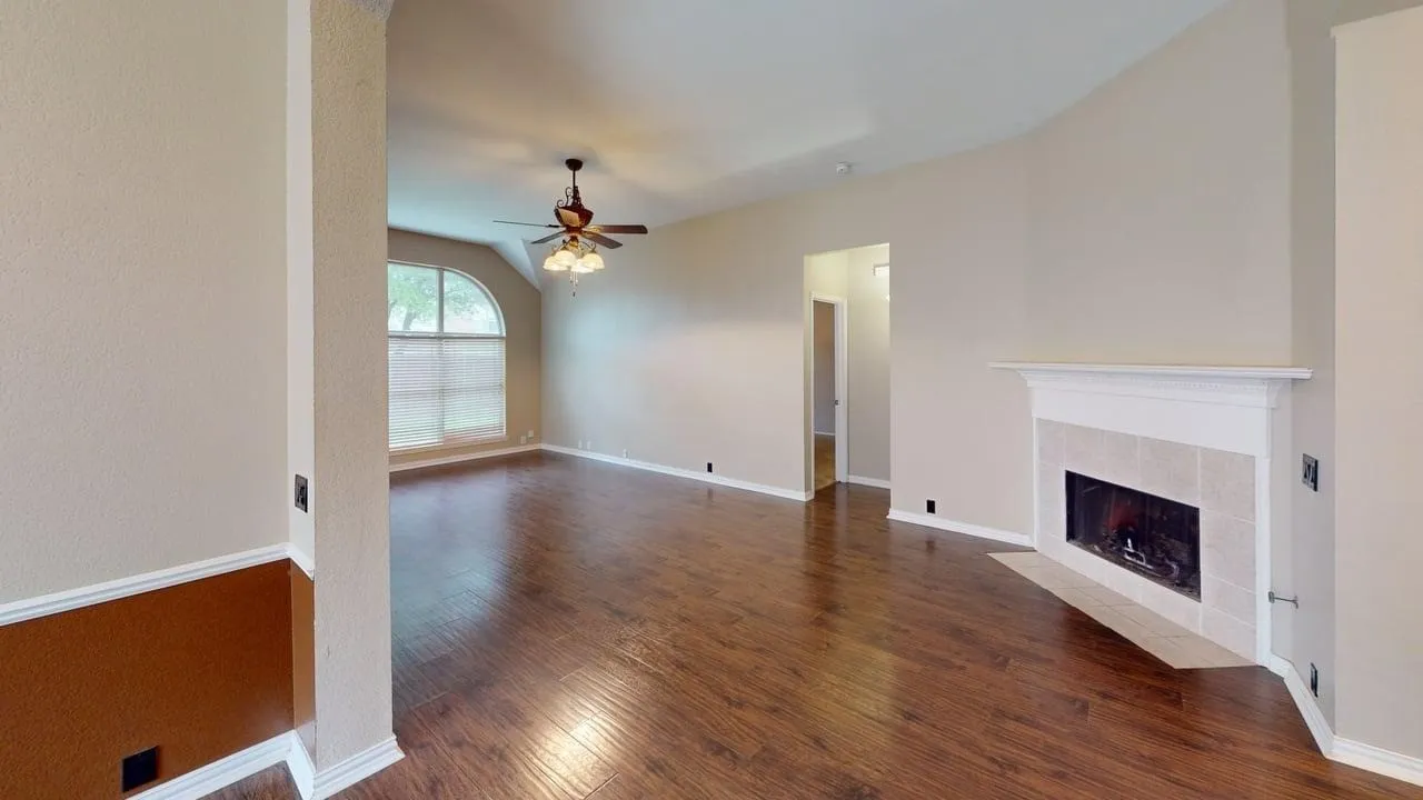 Spacious living area featuring wood-finish flooring, a corner fireplace with a tiled surround and white mantel, and vaulted ceilings