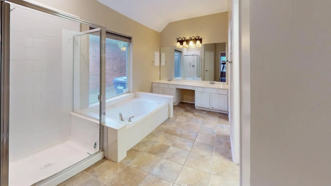 Spacious bathroom featuring a built-in jetted tub, separate glass-enclosed shower, dual vanity with undermount sinks, tile flooring, and vaulted ceiling