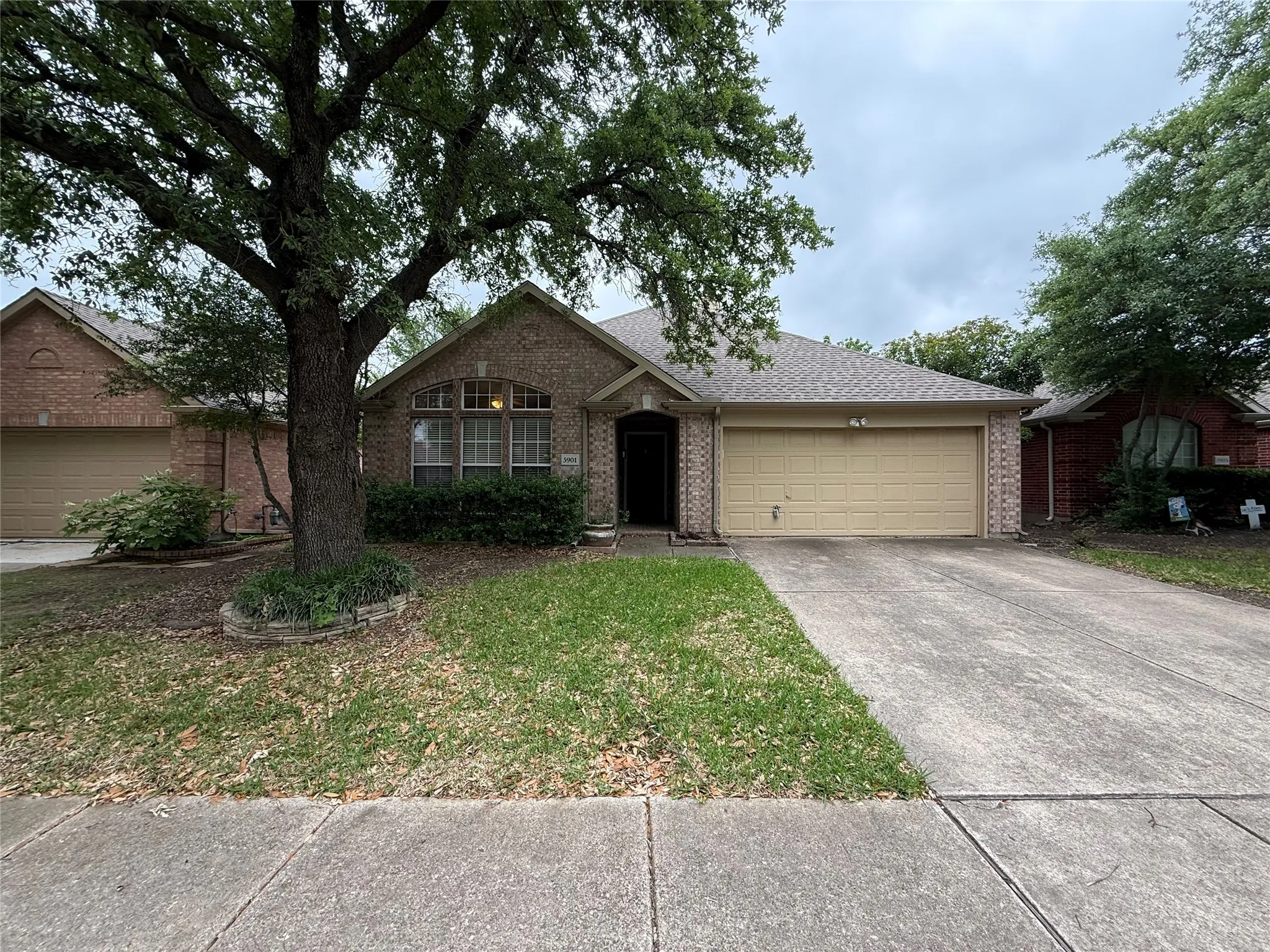 Brick facade home featuring a two-car garage, mature tree, and concrete driveway