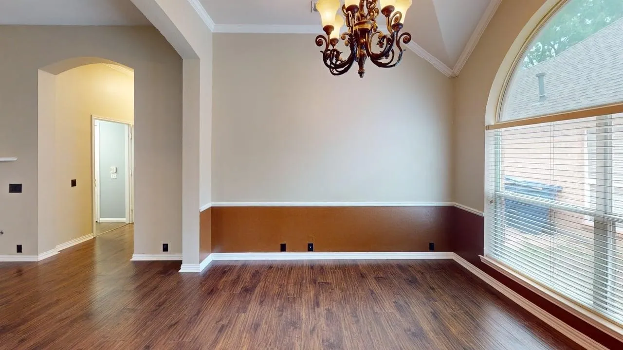 Spacious room featuring wood-finish flooring, a decorative chandelier, and an arched window with blinds