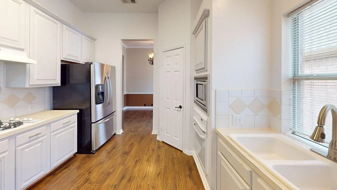 Kitchen featuring white cabinetry, wood-finish flooring, white tiled backsplash, stainless steel appliances, and a double basin sink