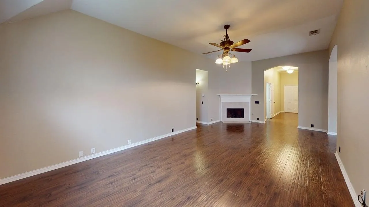 Spacious interior featuring wood-finish flooring, a vaulted ceiling, and a fireplace with a white mantel