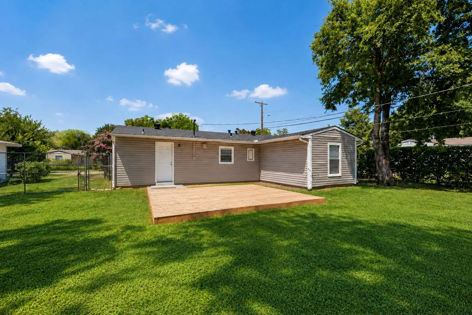 Spacious backyard featuring a new wooden deck, expansive lawn, and a privacy hedge