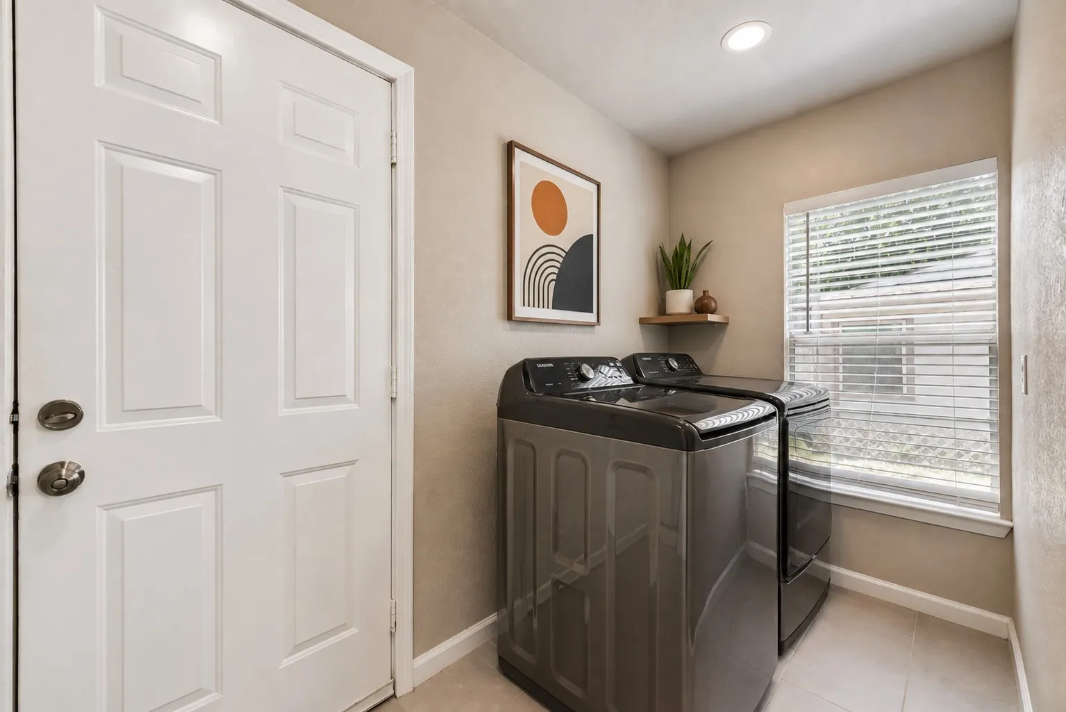 Dedicated laundry area featuring a window with horizontal blinds, recessed lighting, tile flooring, and a floating wood-finish shelf
