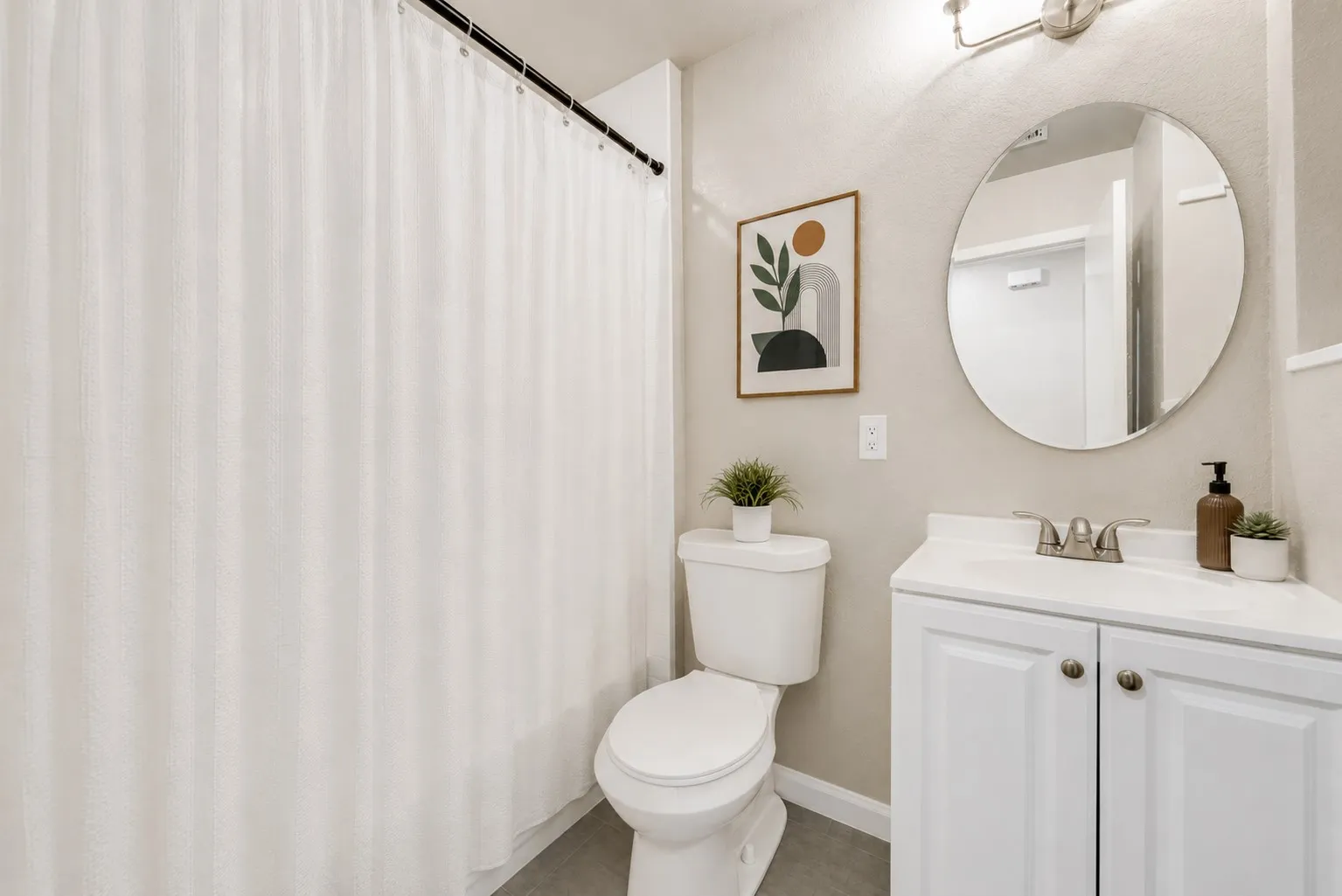 Bathroom featuring a white vanity with an integrated sink, brushed nickel faucet, and a circular mirror