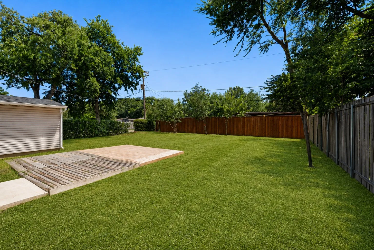Expansive green lawn featuring a wood privacy fence, mature trees, and a concrete patio pad