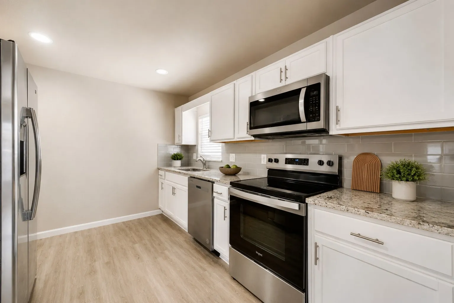 Kitchen featuring white cabinetry with silver hardware, granite countertops, stainless steel appliances, a subway tile backsplash, and wood-finish flooring