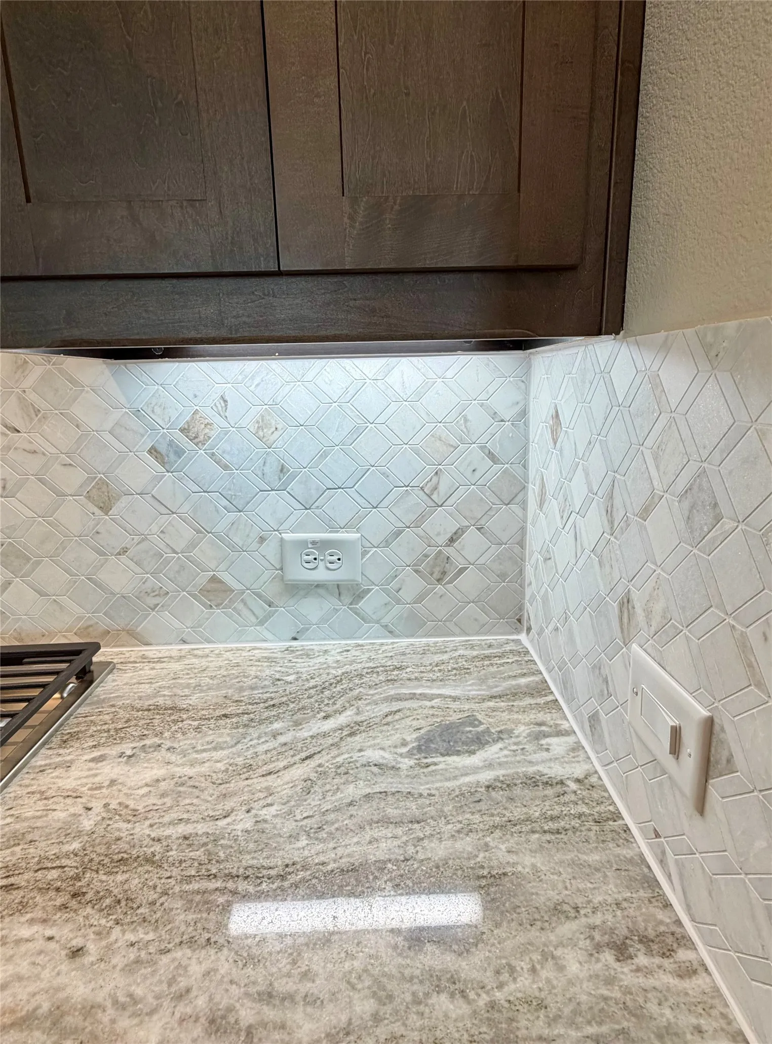 Brownstone Shaker cabinets, undercabinet lights, decorative mosaic tile backsplash, and Fantasy Brown granite counters