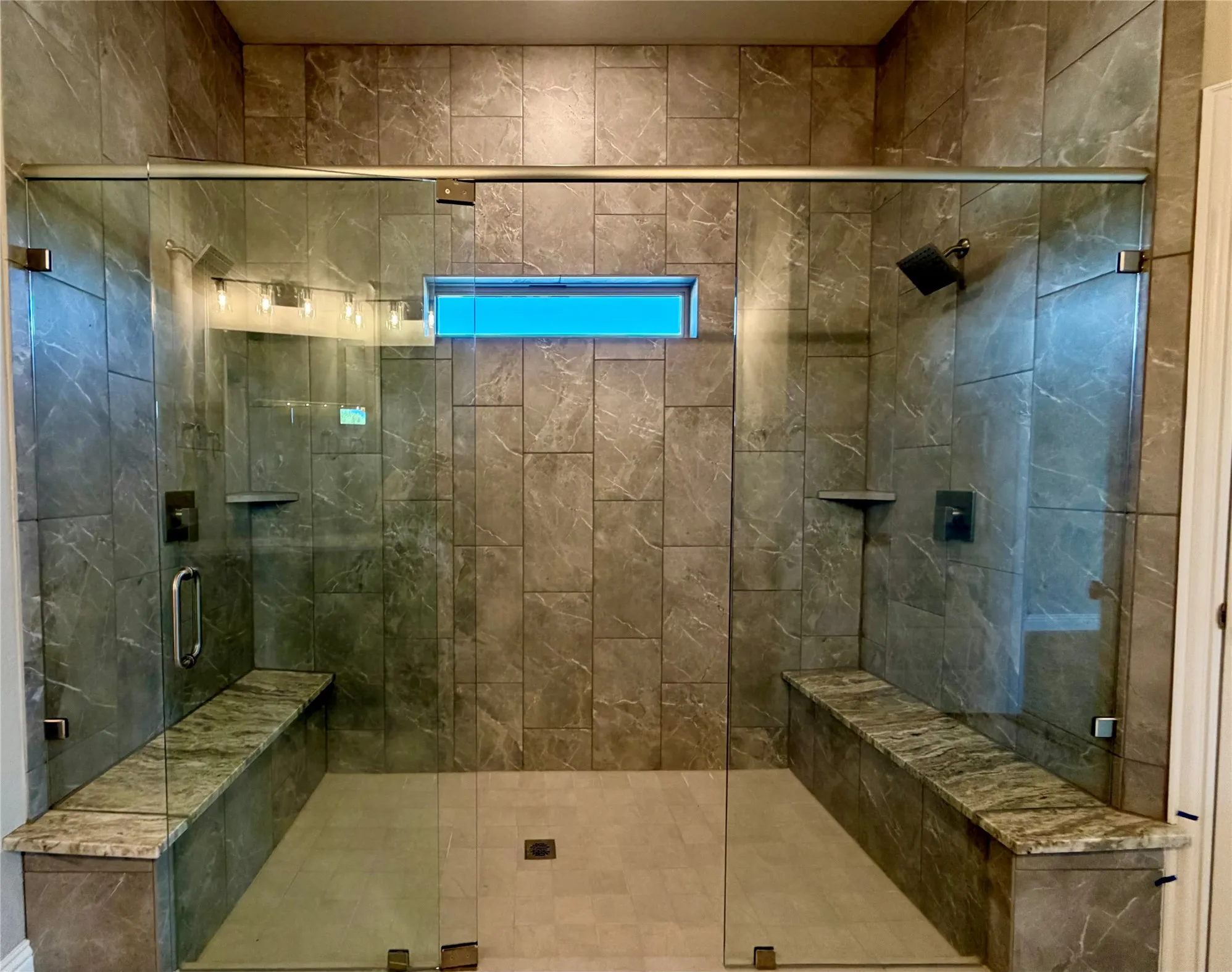 Enormous master shower with accent tile to ceiling, 2 benches, and 2 shower heads