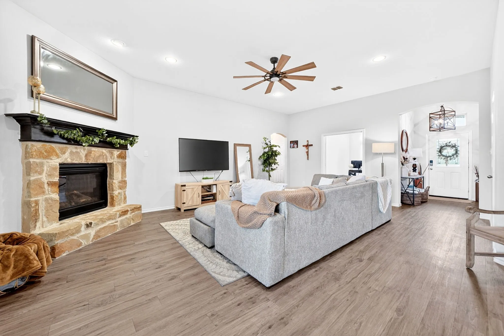 Living area featuring a corner stone fireplace with a dark wood mantel, recessed lighting, a ceiling fan with wood-tone blades, and wood-finish flooring