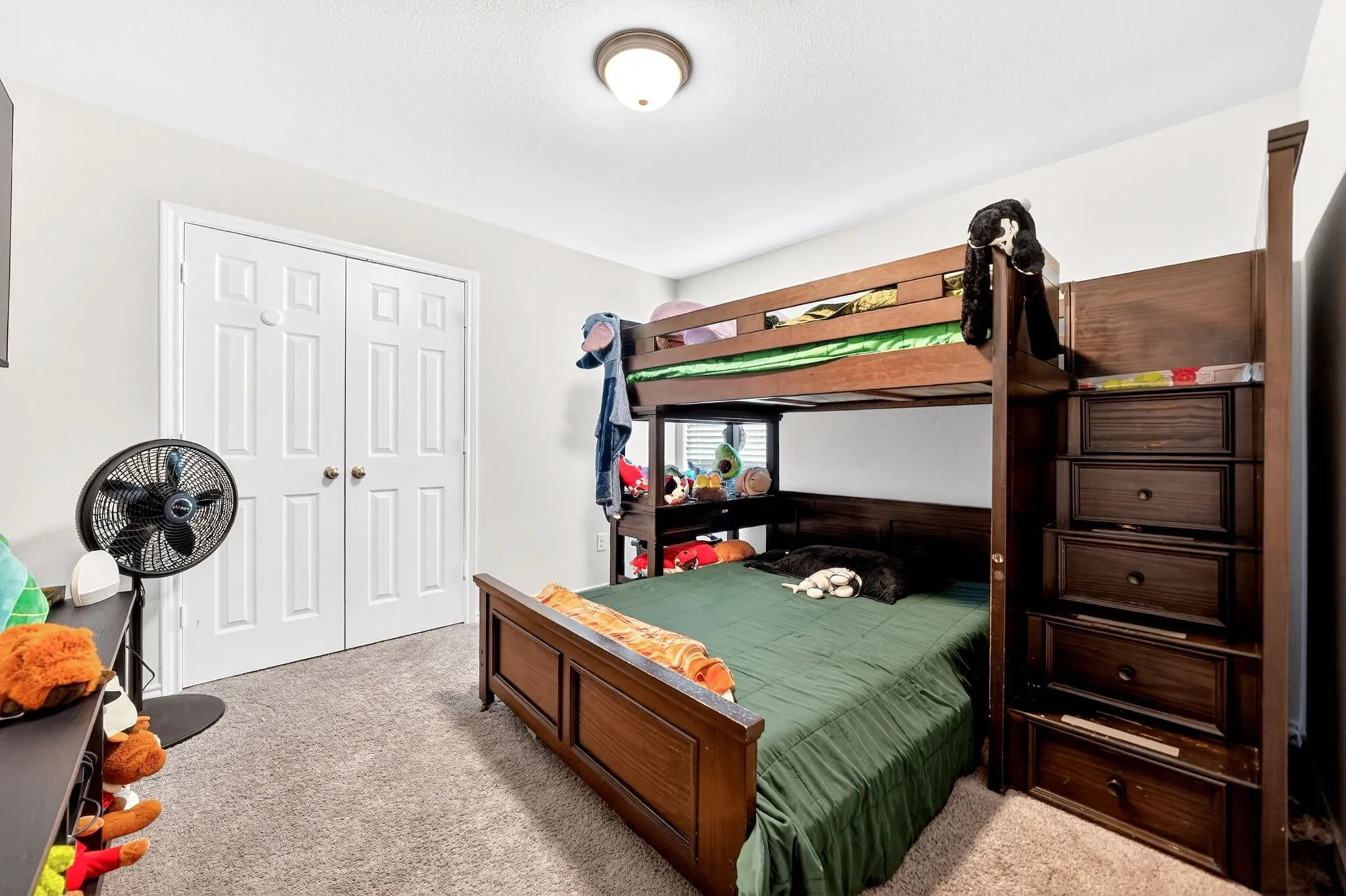 Spacious bedroom featuring dark wood bunk bed with built-in storage shelving, wood-finish flooring, ceiling-mounted light fixture, and ample closet space with dual doors