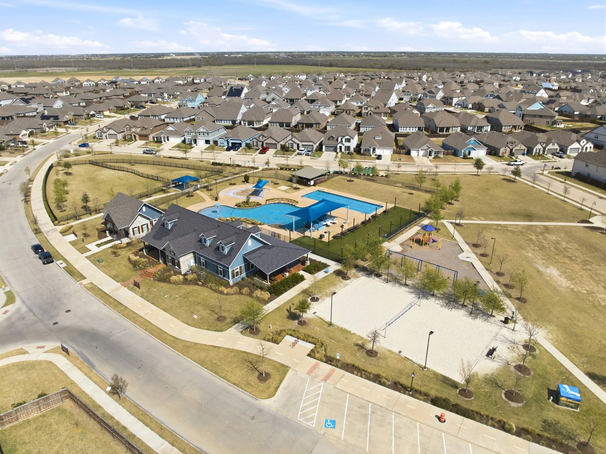 Aerial view of this residential community featuring a striking home with a dark exterior and expansive blue recreational amenity