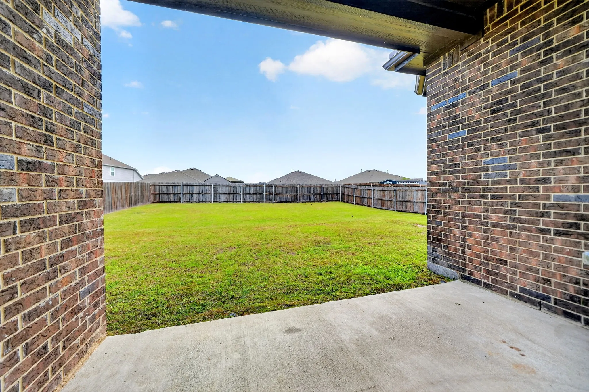 Expansive backyard with lush, manicured lawn framed by mature brick construction