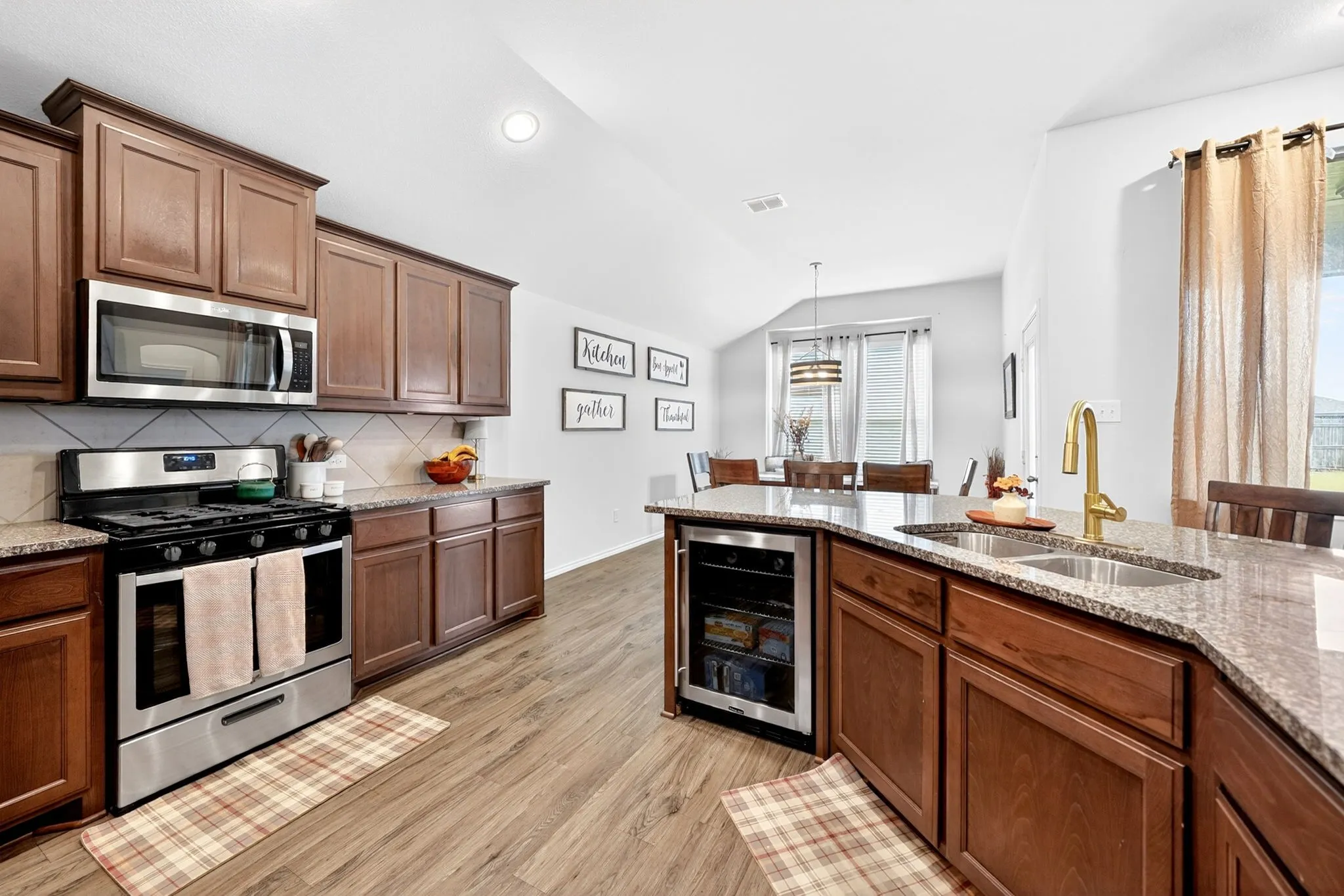 Spacious kitchen featuring rich wood cabinetry, stainless steel appliances, and a large center island with wood-finish flooring throughout