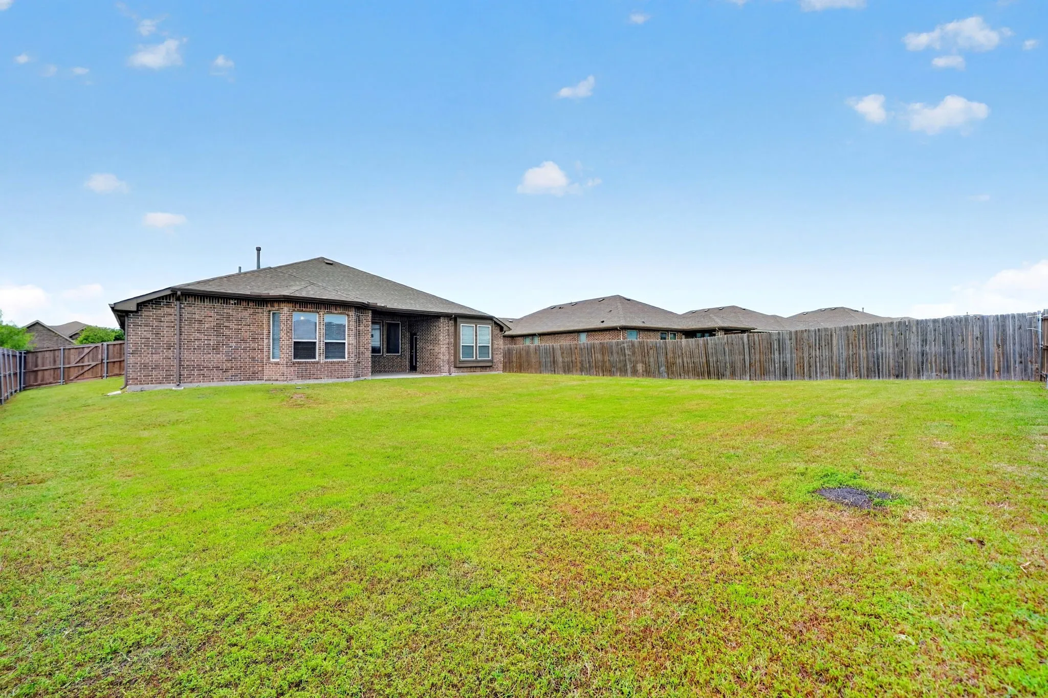 Brick residence situated on expansive grounds featuring a wide-open lawn, wooden perimeter fencing, and multiple outbuildings