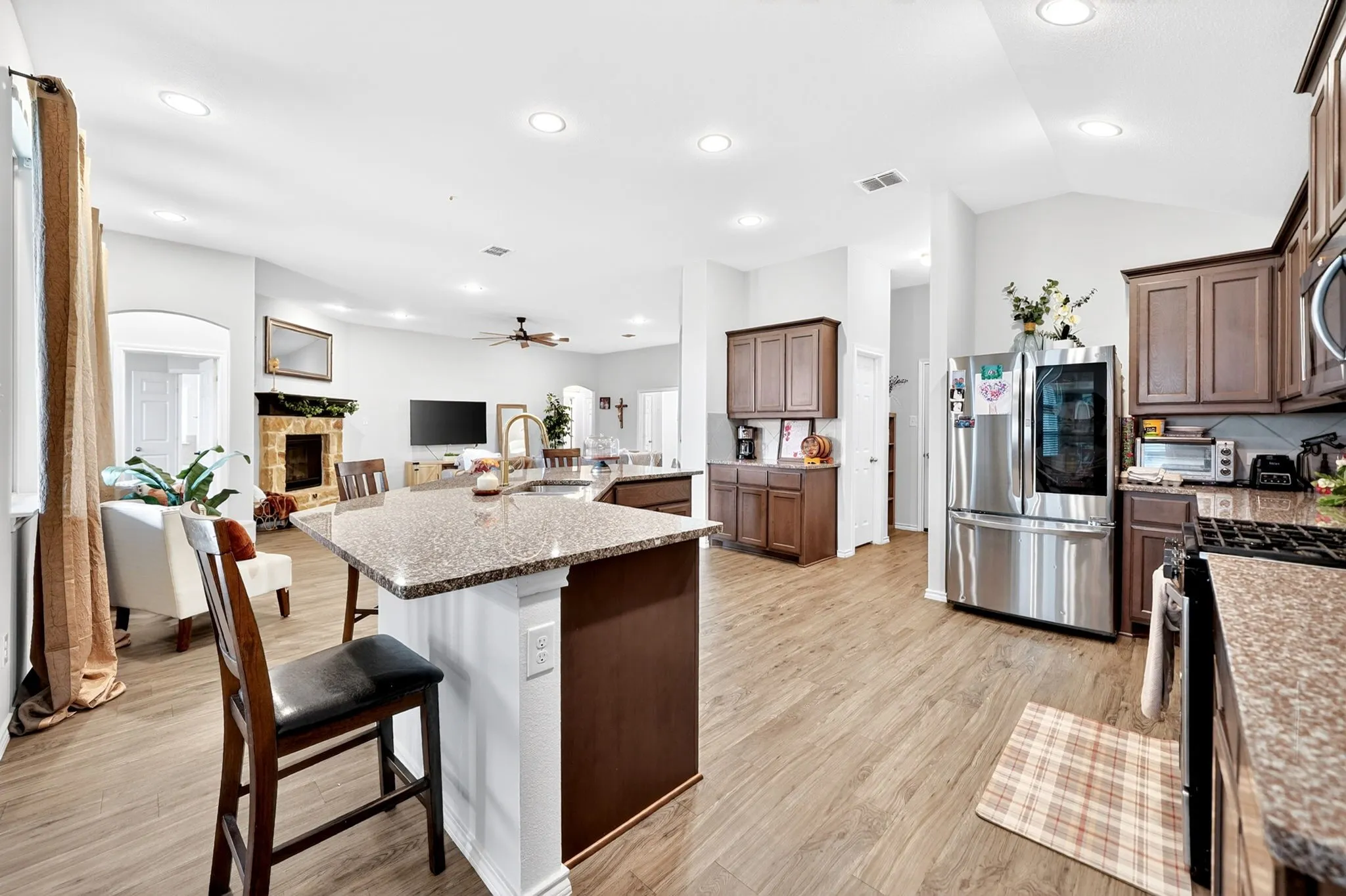 Expansive kitchen featuring a large island with a stone-finish countertop, stainless steel appliances, wood-finish flooring, recessed lighting, and rich wood cabinetry
