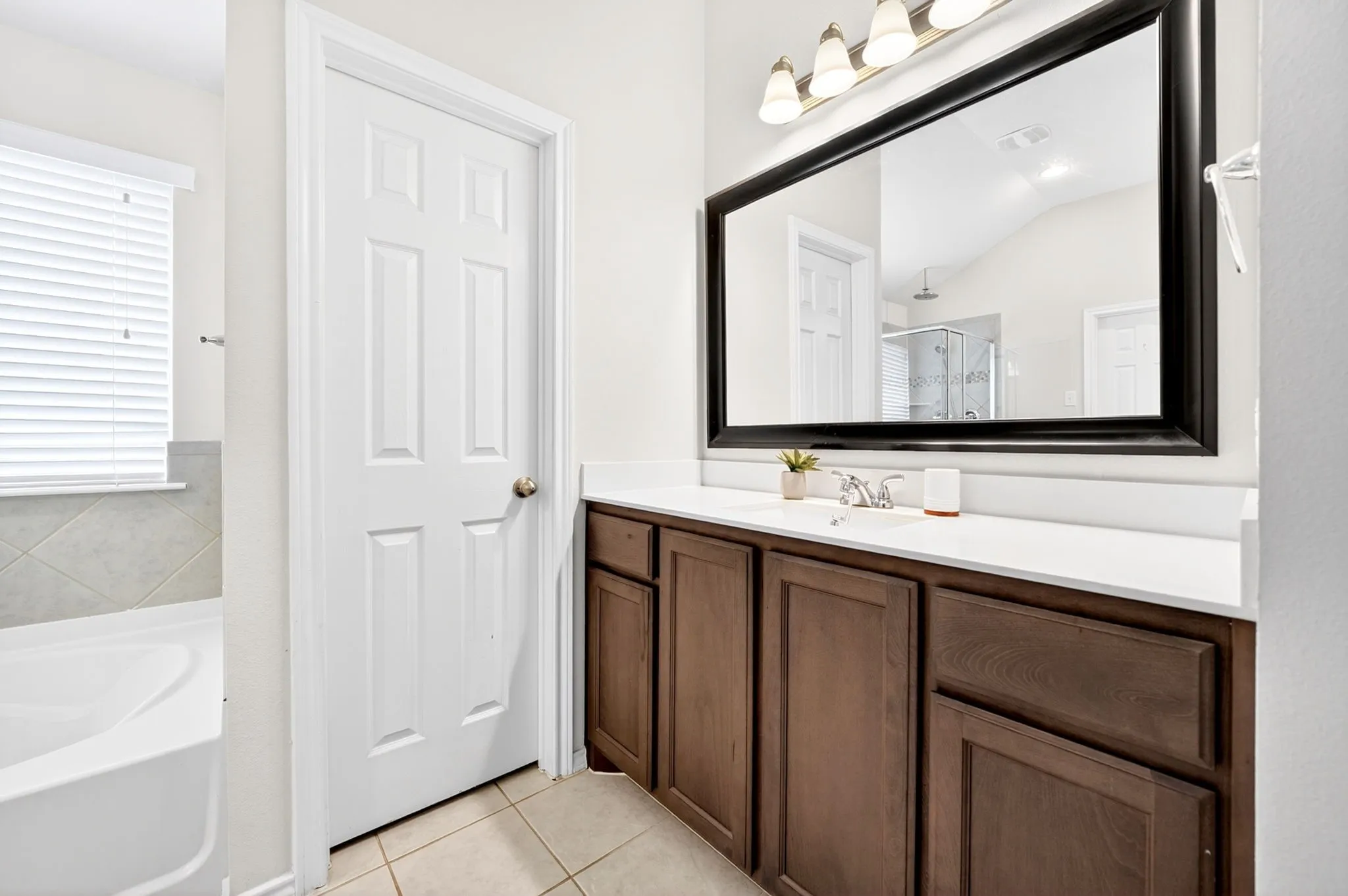 Elegant master bathroom featuring a dark wood vanity with dual sink preparation, white marble countertop, and an oversized framed mirror illuminated by chrome sconces