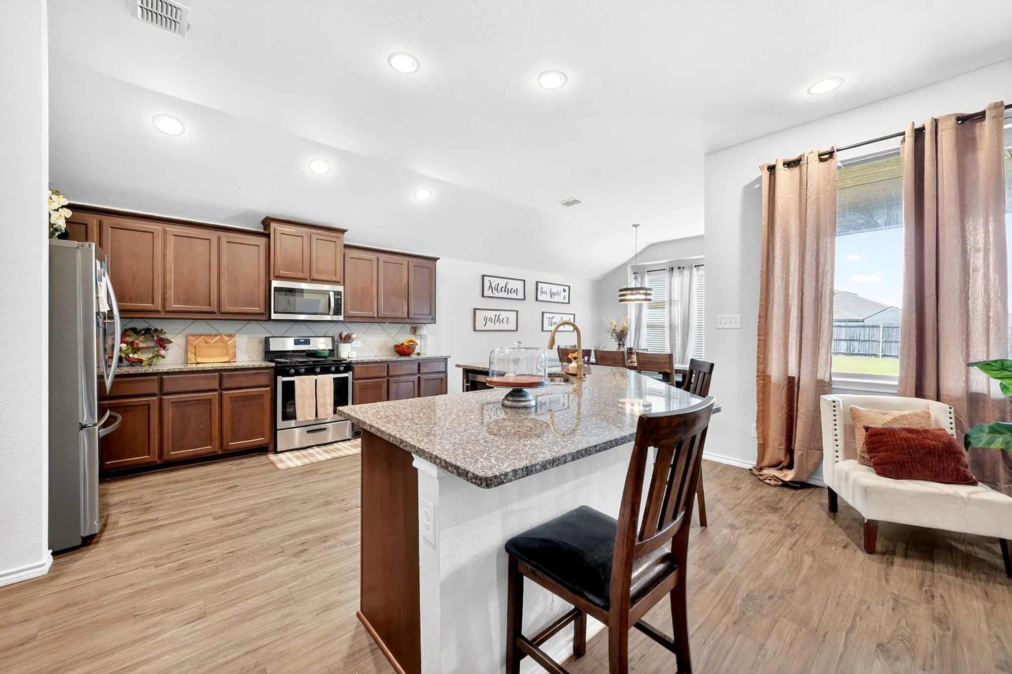 Open-concept kitchen and dining area featuring rich wood cabinetry, stainless steel appliances, and a granite-topped island with seating