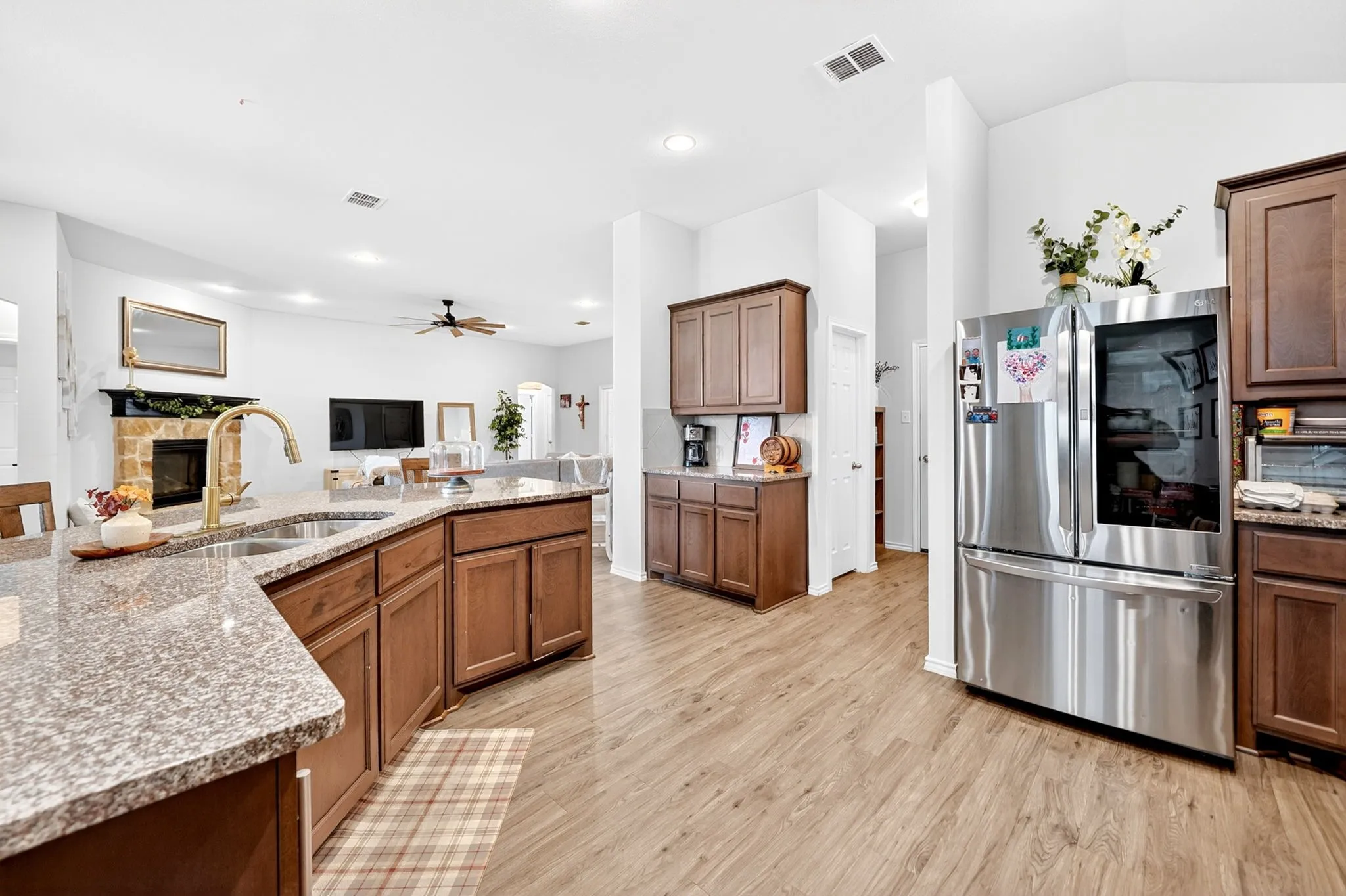 Open-concept kitchen featuring warm wood-finish cabinetry, granite countertops, a spacious island with seating, and stainless steel appliances including a French-door refrigerator