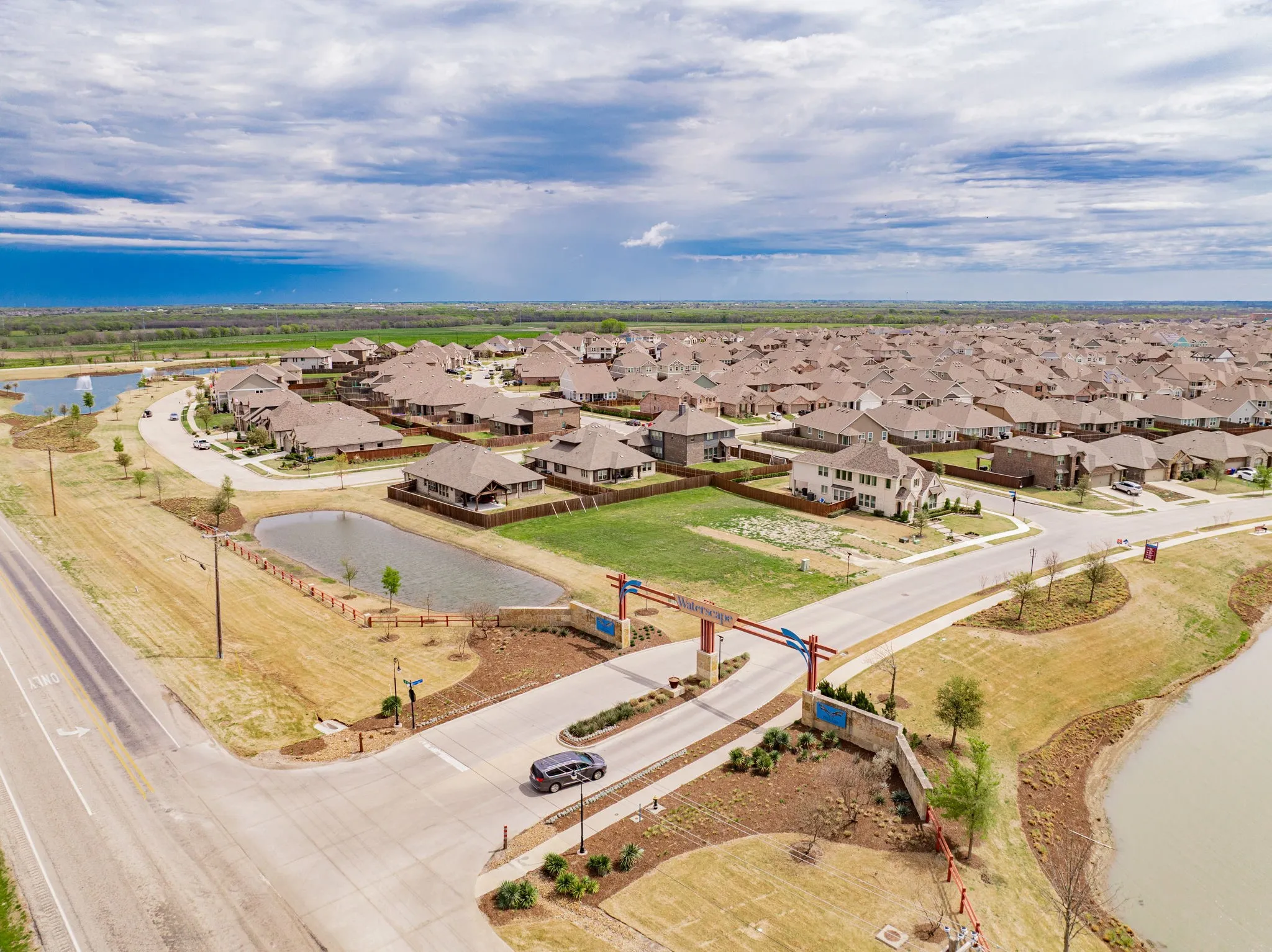 Aerial view of a sprawling residential community featuring multiple single-family homes with brick and tan exteriors, manicured lawns, and established landscaping