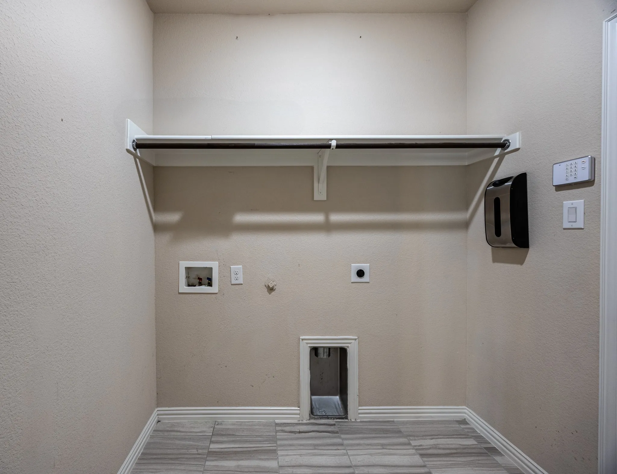 Laundry area featuring a hanging rod, wall-mounted shelf, utility hookups, and patterned tile flooring