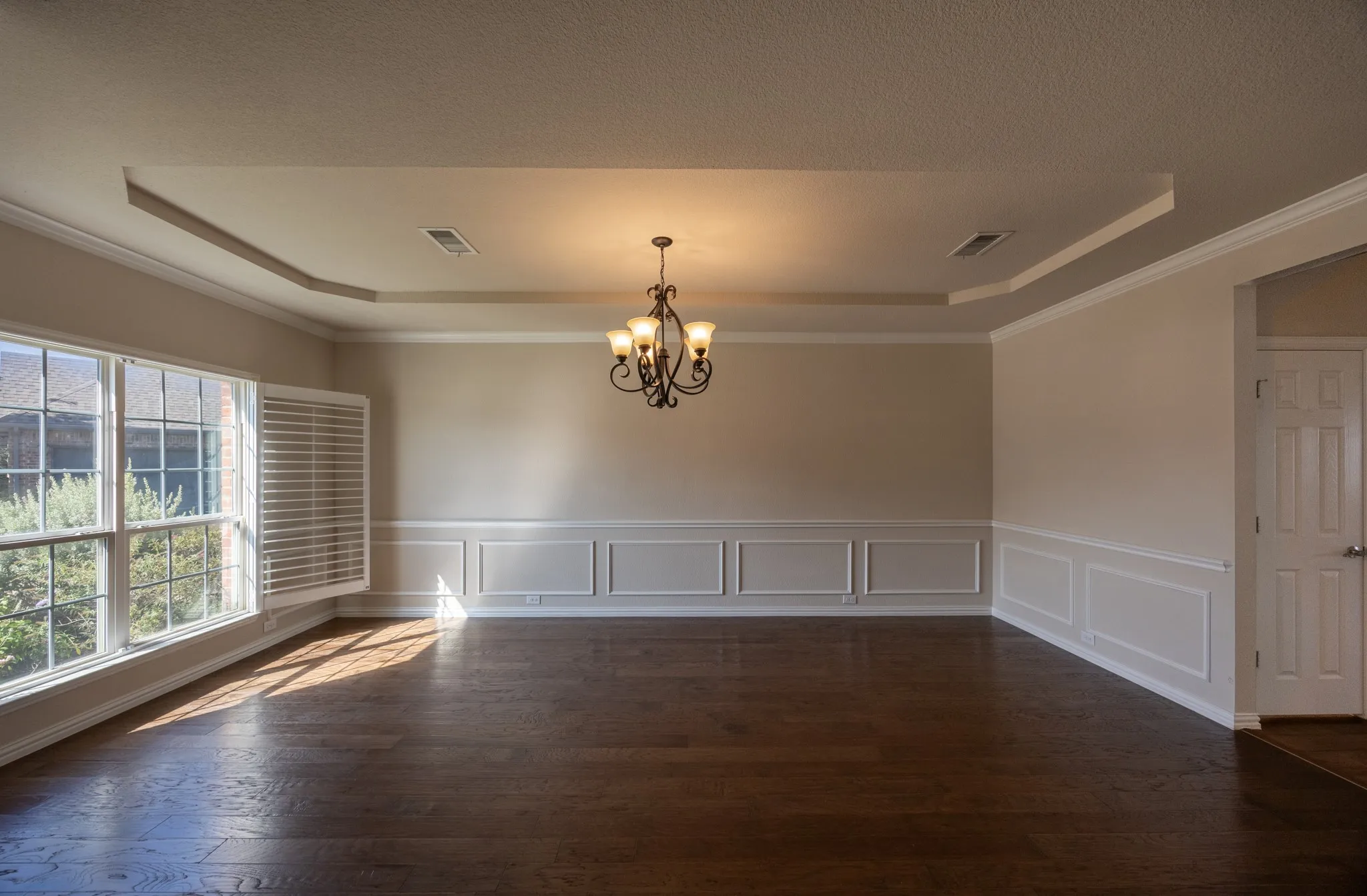 Formal dining space featuring dark wood-finish flooring, wainscoting, and crown molding