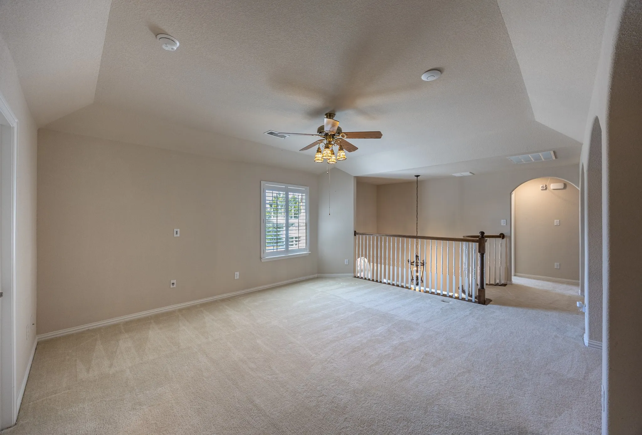 Spacious room with vaulted ceiling and neutral carpet flooring