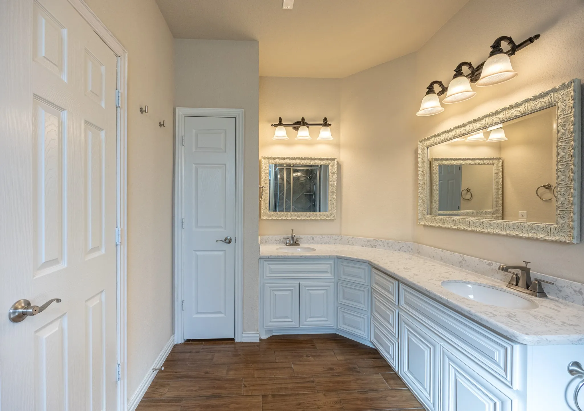 Bathroom featuring a dual vanity with white cabinetry and light-toned countertops, two framed mirrors, and wood-finish flooring