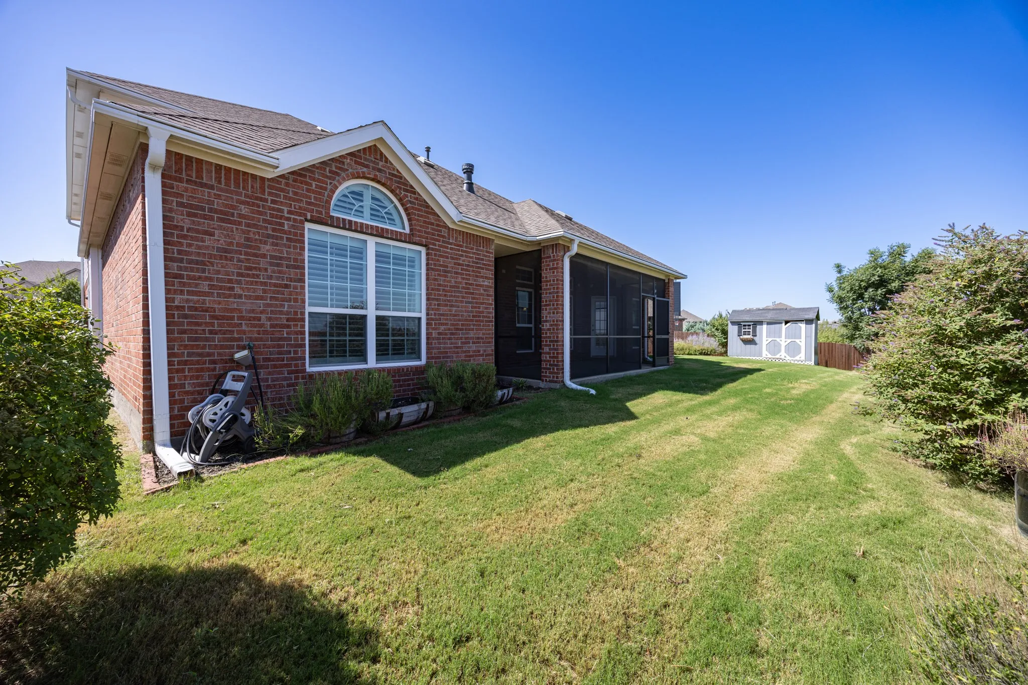 Expansive backyard featuring a manicured lawn, brick exterior, screened patio, and storage shed