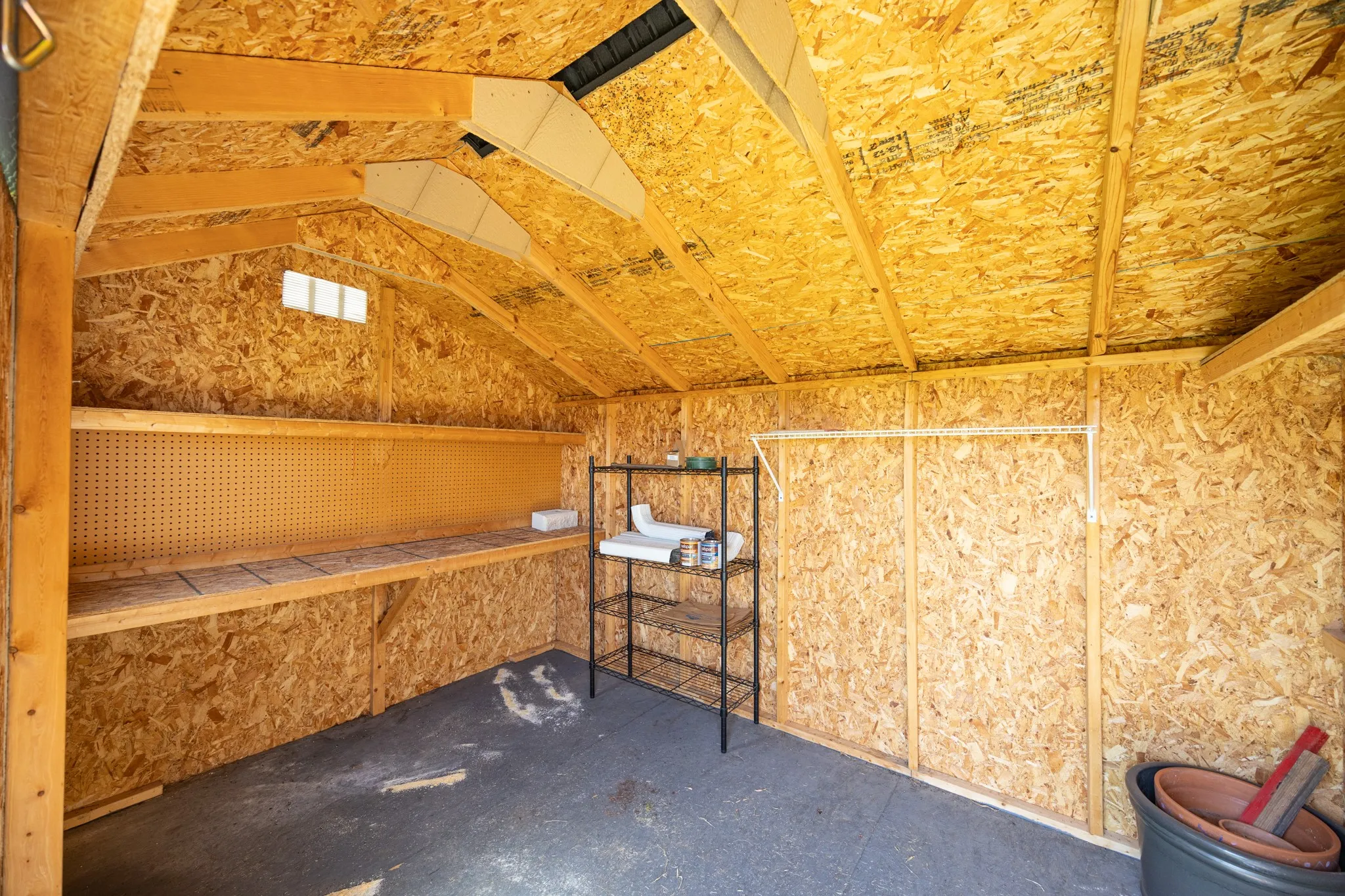 Interior shed space featuring exposed wood framing, built-in shelving, pegboard backing, and a concrete floor