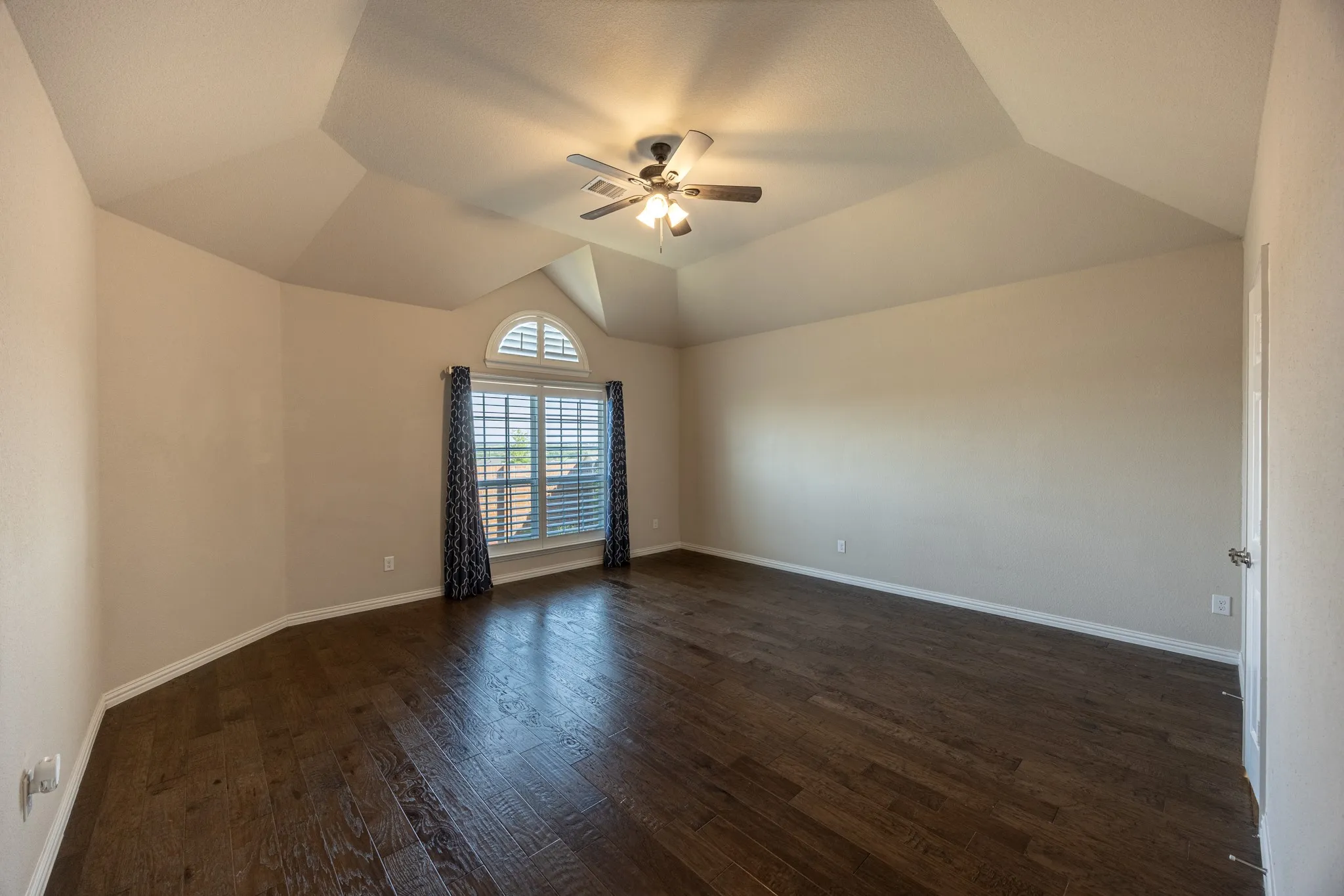 Spacious room featuring wood-finish flooring, a tray ceiling, and a ceiling fan with light fixture