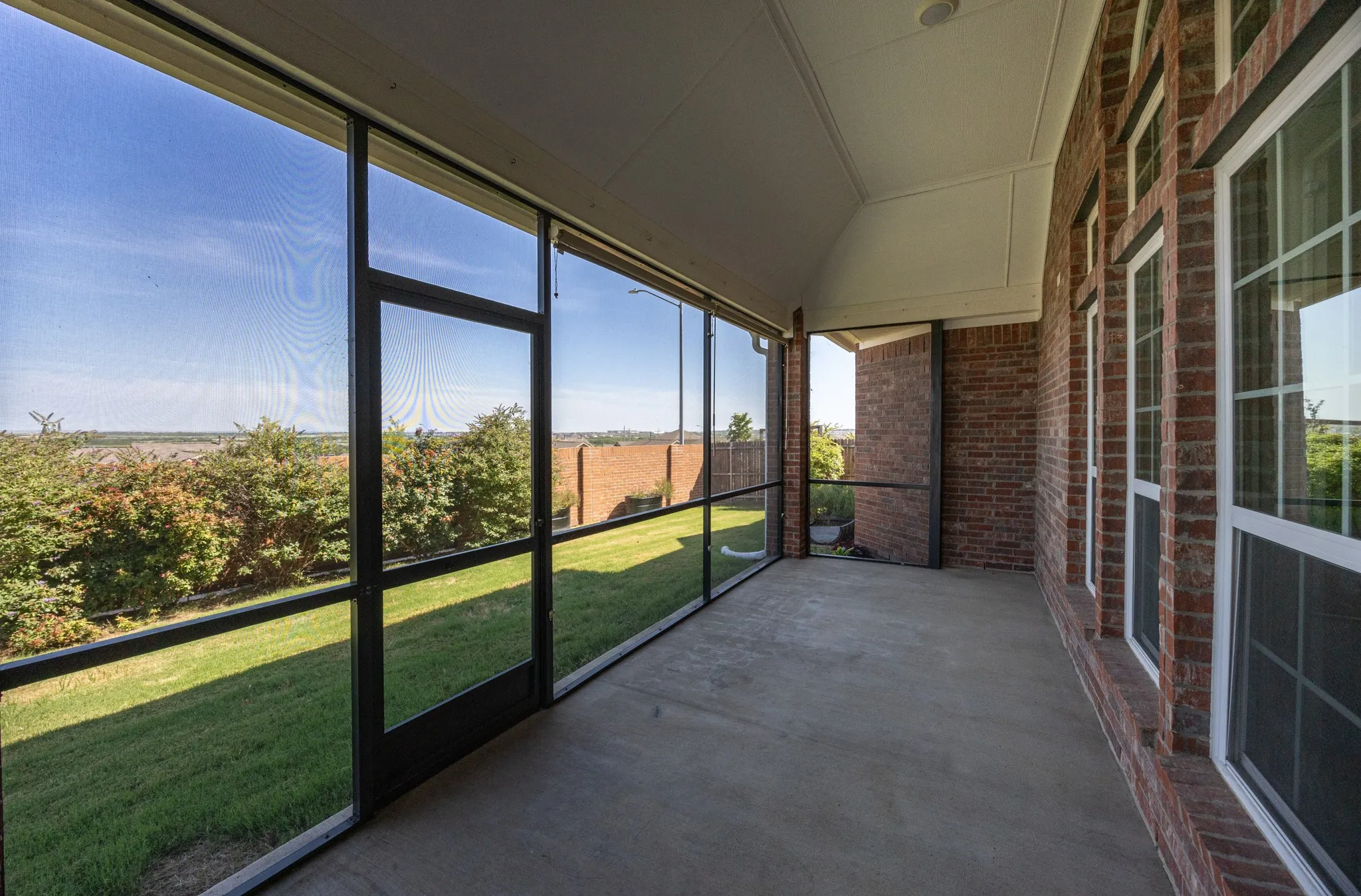 Screened-in porch featuring a concrete floor, vaulted ceiling, and brick exterior wall