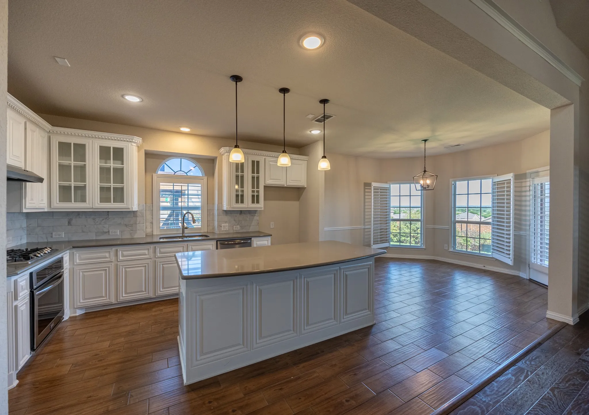 Spacious kitchen featuring white cabinetry, a large island with pendant lighting, stone countertops, and wood-finish flooring