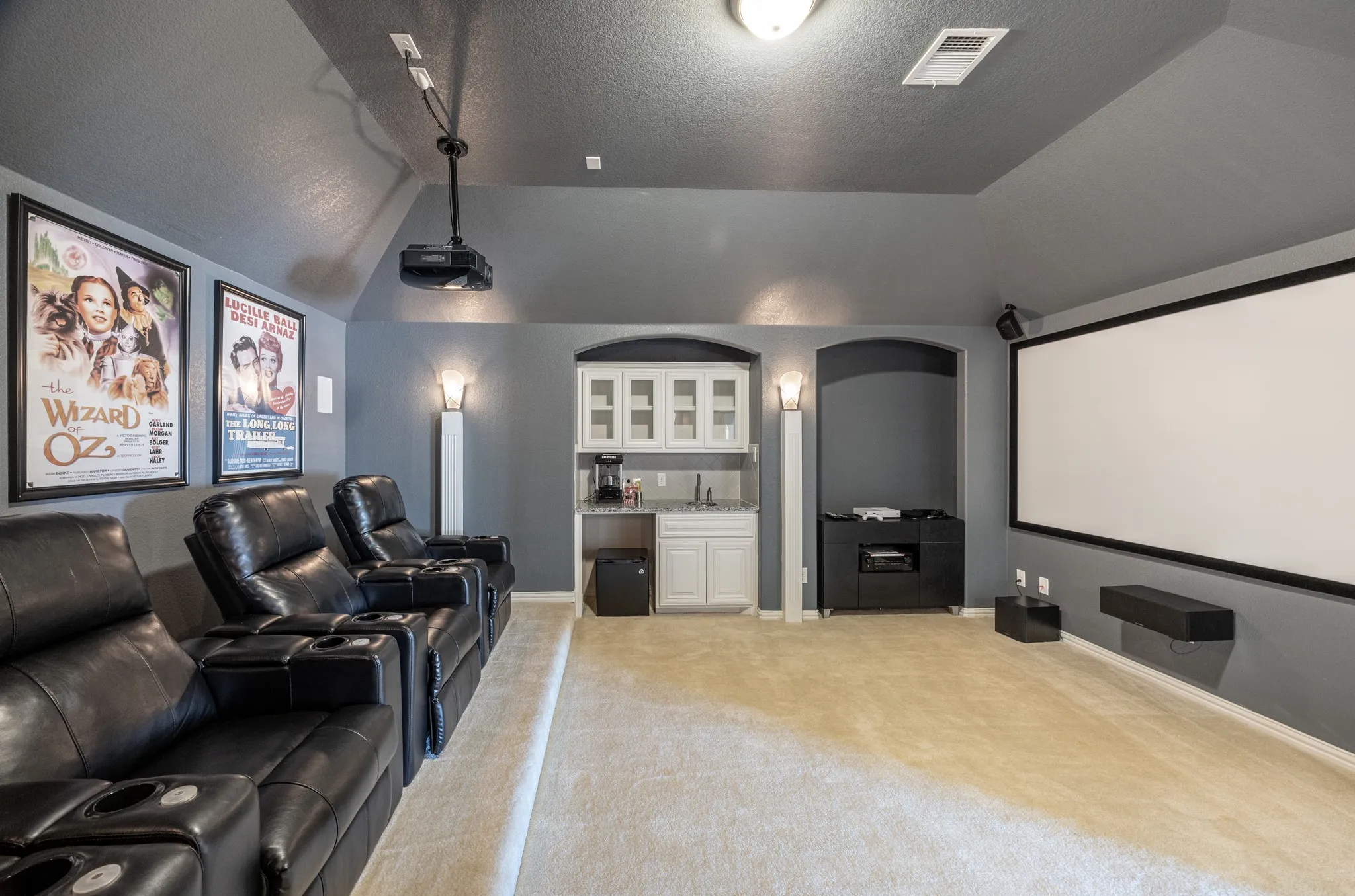 Dedicated media room featuring a large projector screen, mounted projector, and integrated wet bar