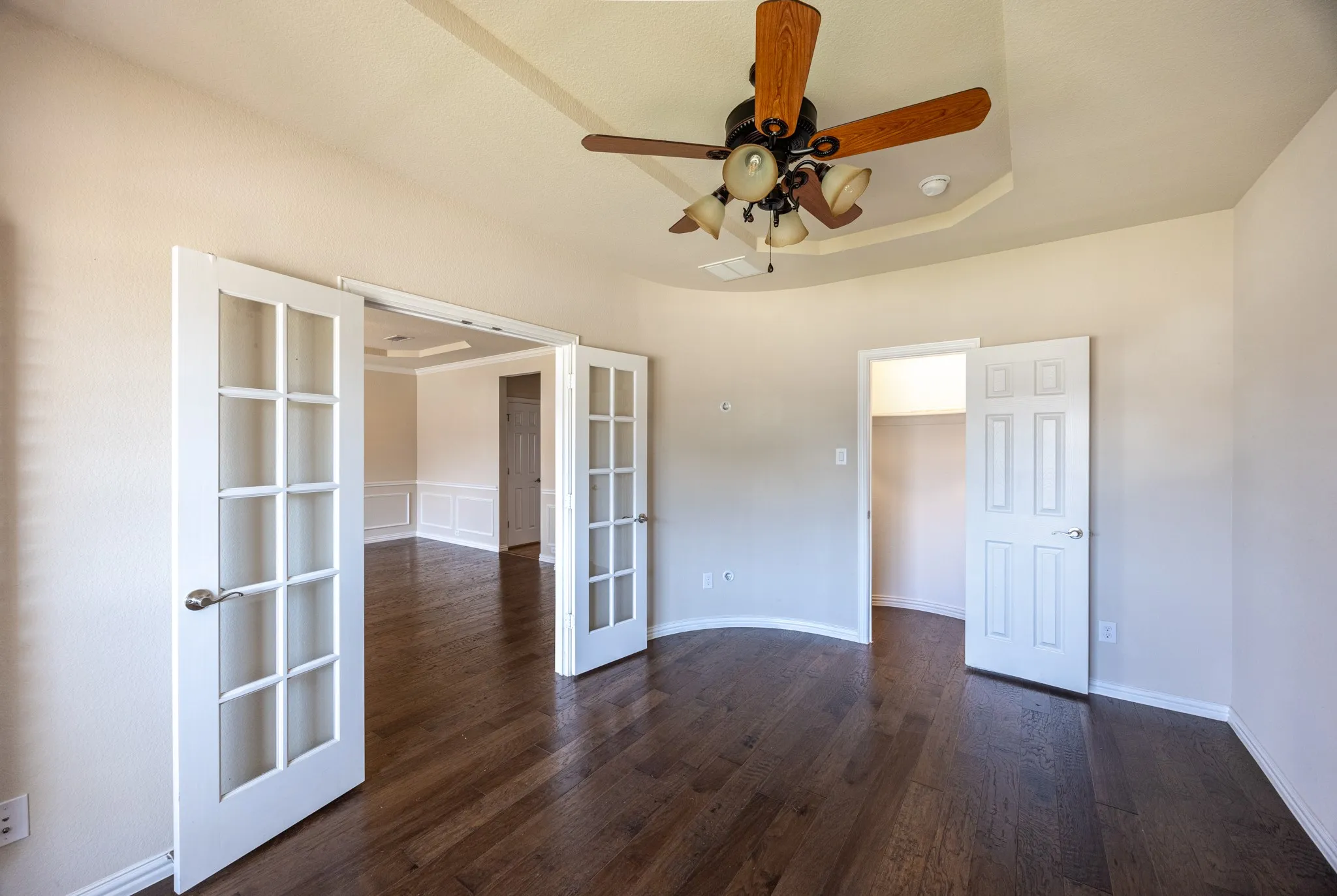 French doors with glass paneling, tray ceiling with a ceiling fan, dark wood-finish flooring, built-in shelving, and neutral wall tones