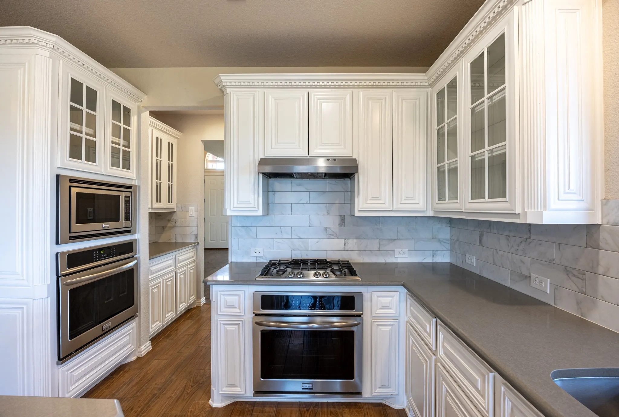 Kitchen featuring white cabinetry with glass-front uppers, stainless steel appliances, a gas cooktop, built-in microwave, and double wall ovens
