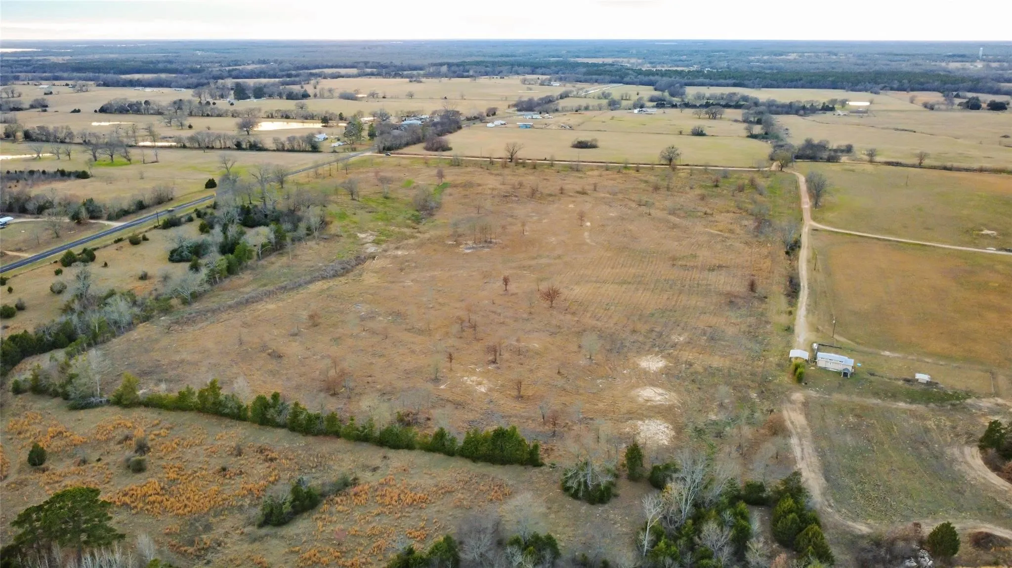 Expansive cleared acreage featuring a perimeter fence line, natural tree borders, and a partial dirt road access