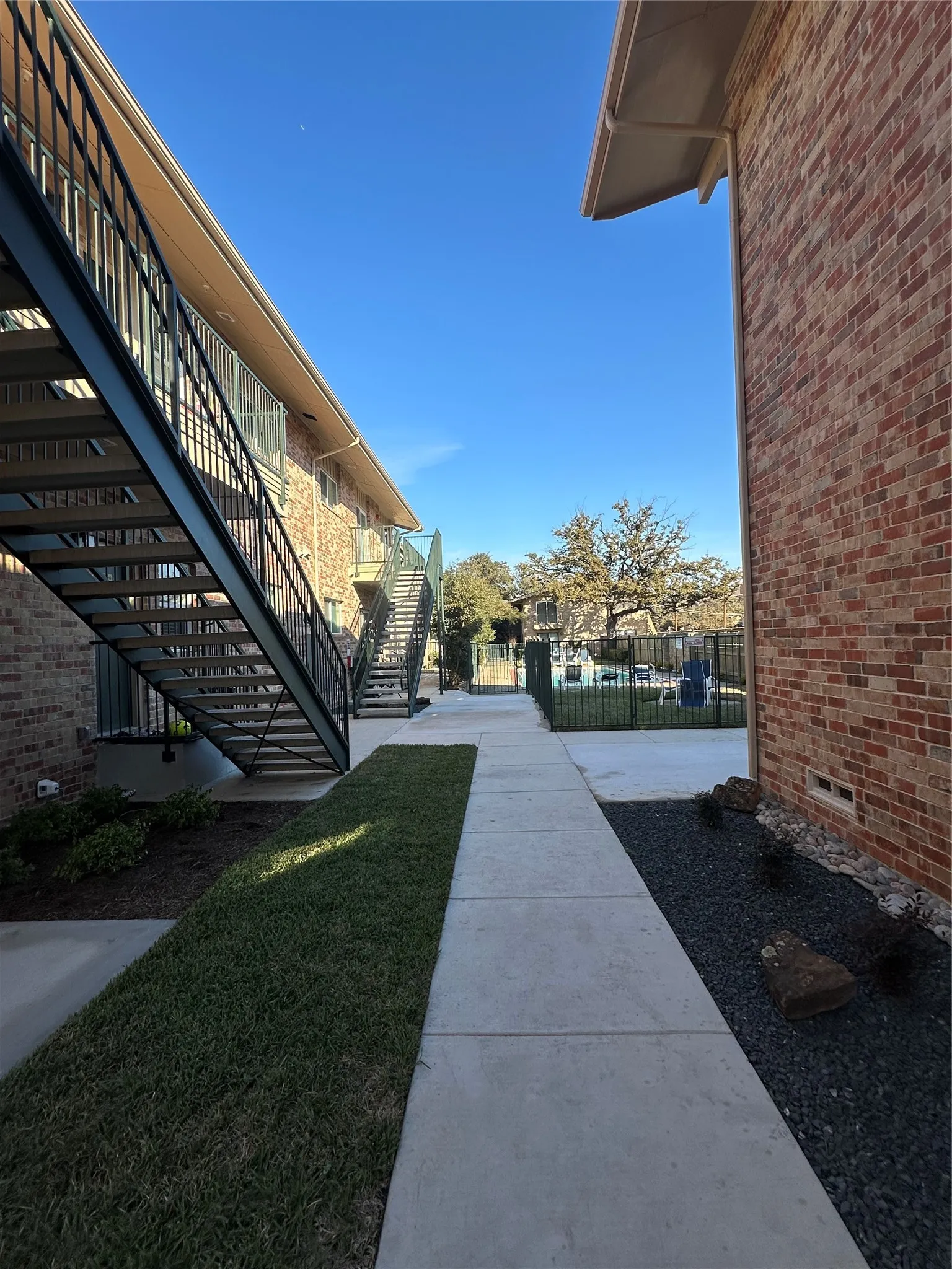 Modern architectural courtyard featuring a clean concrete walkway, manicured lawn with defined landscaping borders, and contemporary metal staircase with geometric railings