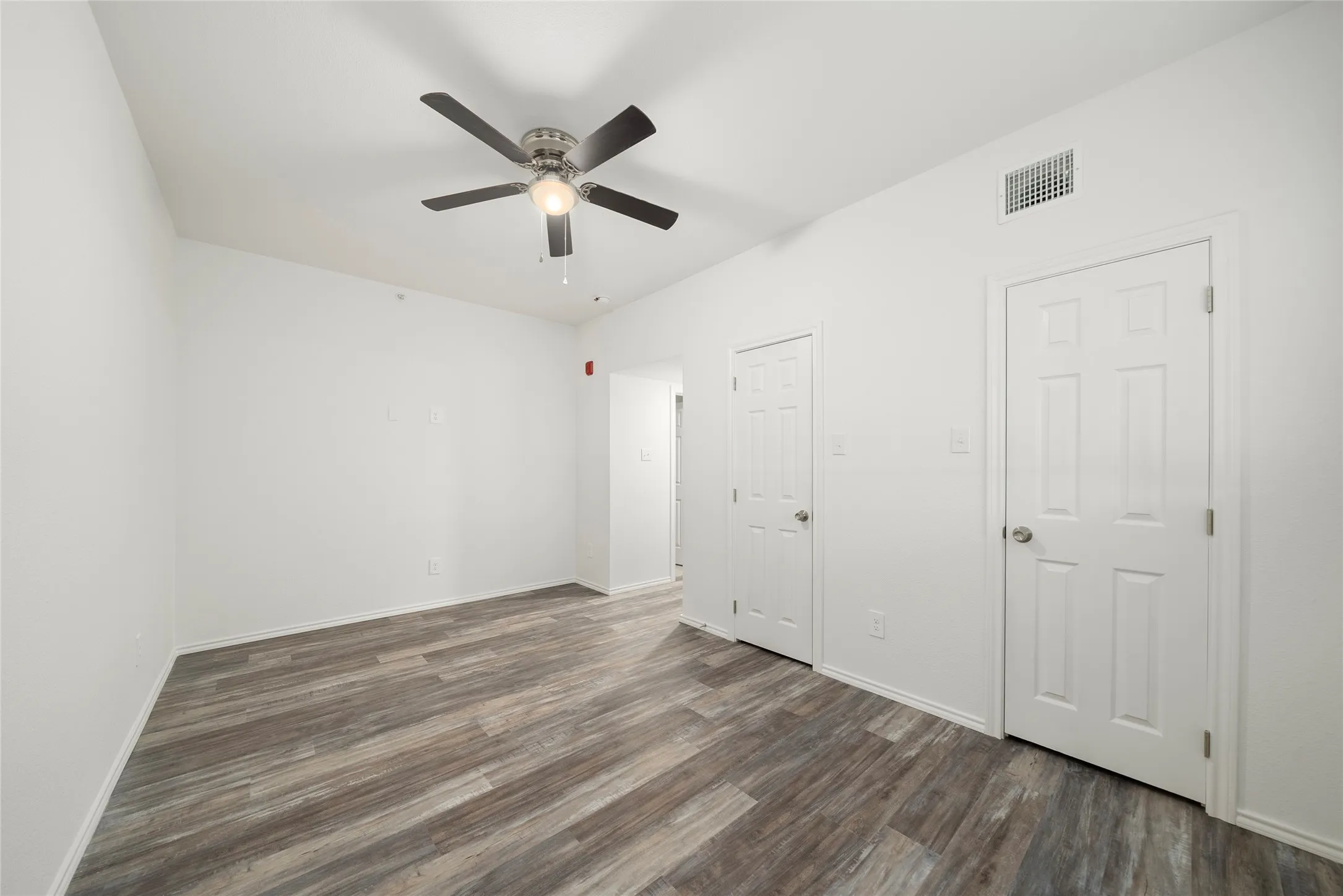 Interior room featuring wood-finish flooring, white walls, and a ceiling fan with integrated lighting
