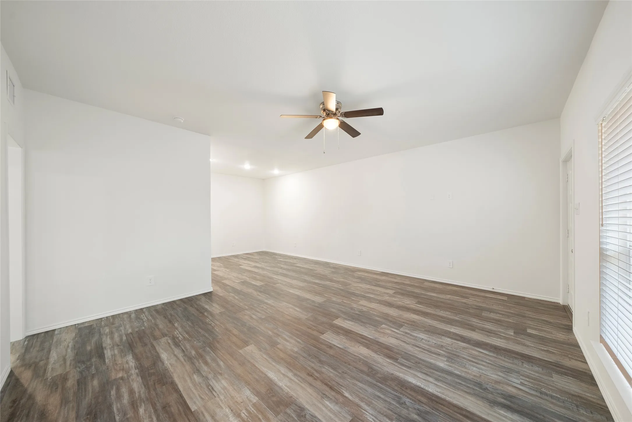 Spacious room with wood-finish flooring, white walls, and a ceiling fan with a brushed metal base