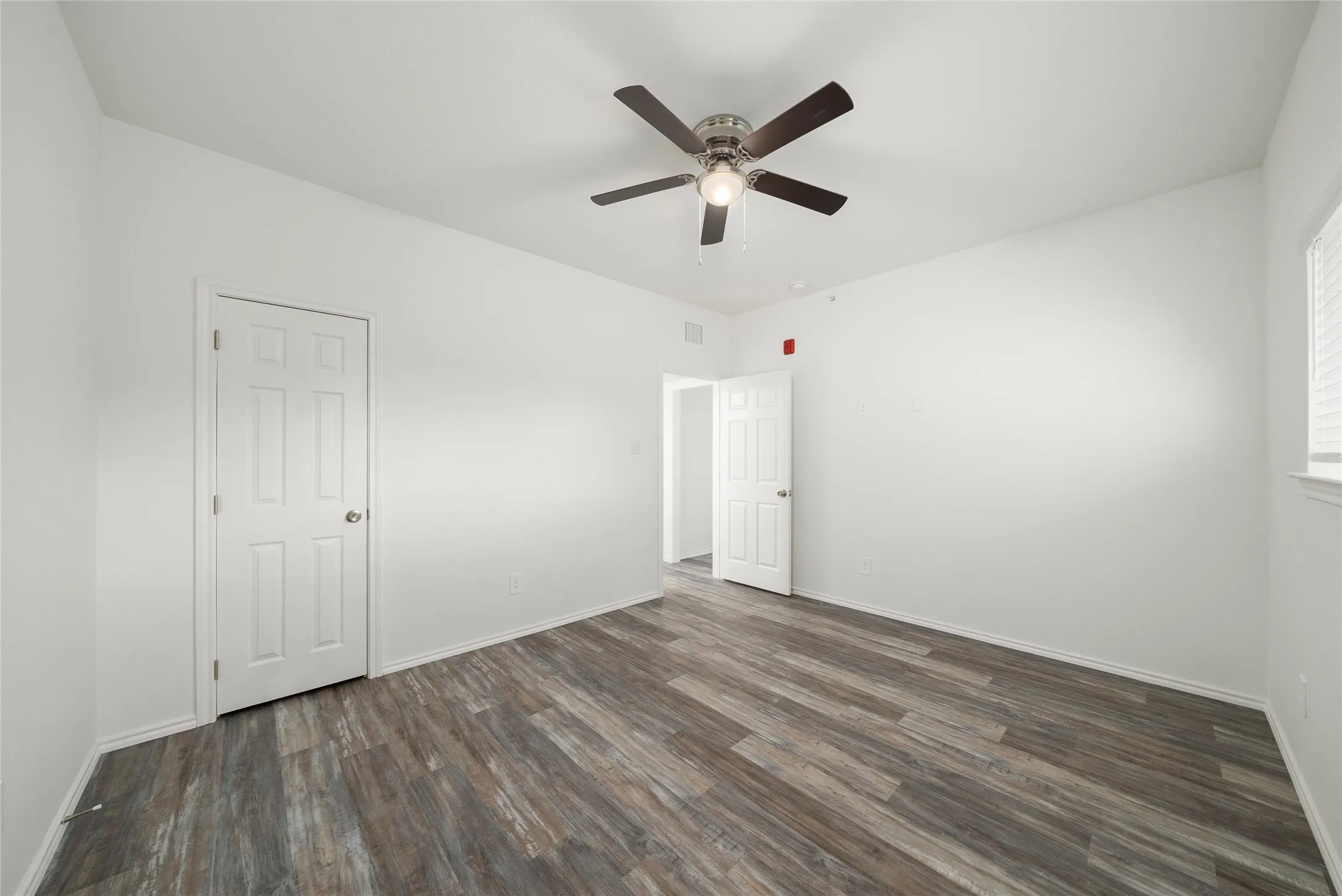Spacious interior featuring wood-finish flooring, white walls, and a ceiling fan with integrated lighting