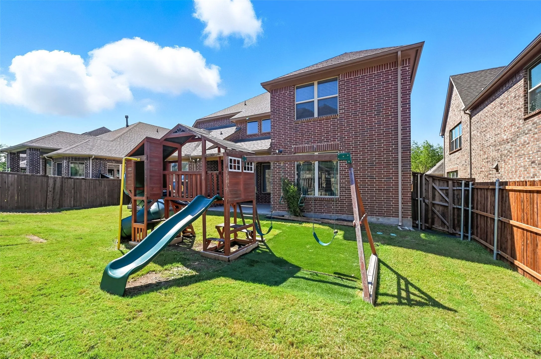 Spacious fenced backyard featuring a substantial play structure, manicured lawn, and brick exterior