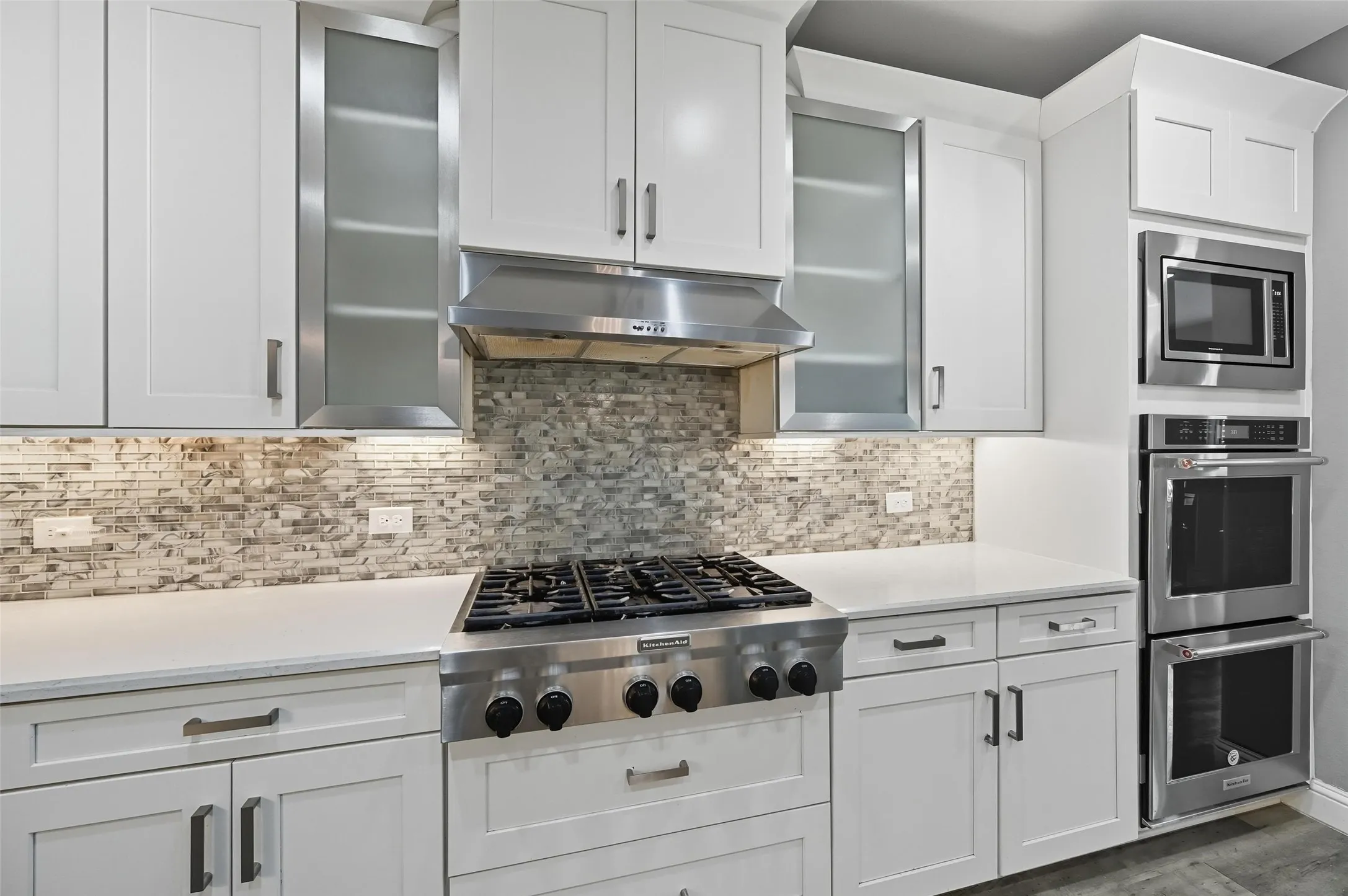 Gourmet kitchen featuring a stainless steel range with a ventilation hood, mosaic tile backsplash, white shaker-style cabinetry, and integrated stainless steel double ovens and microwave