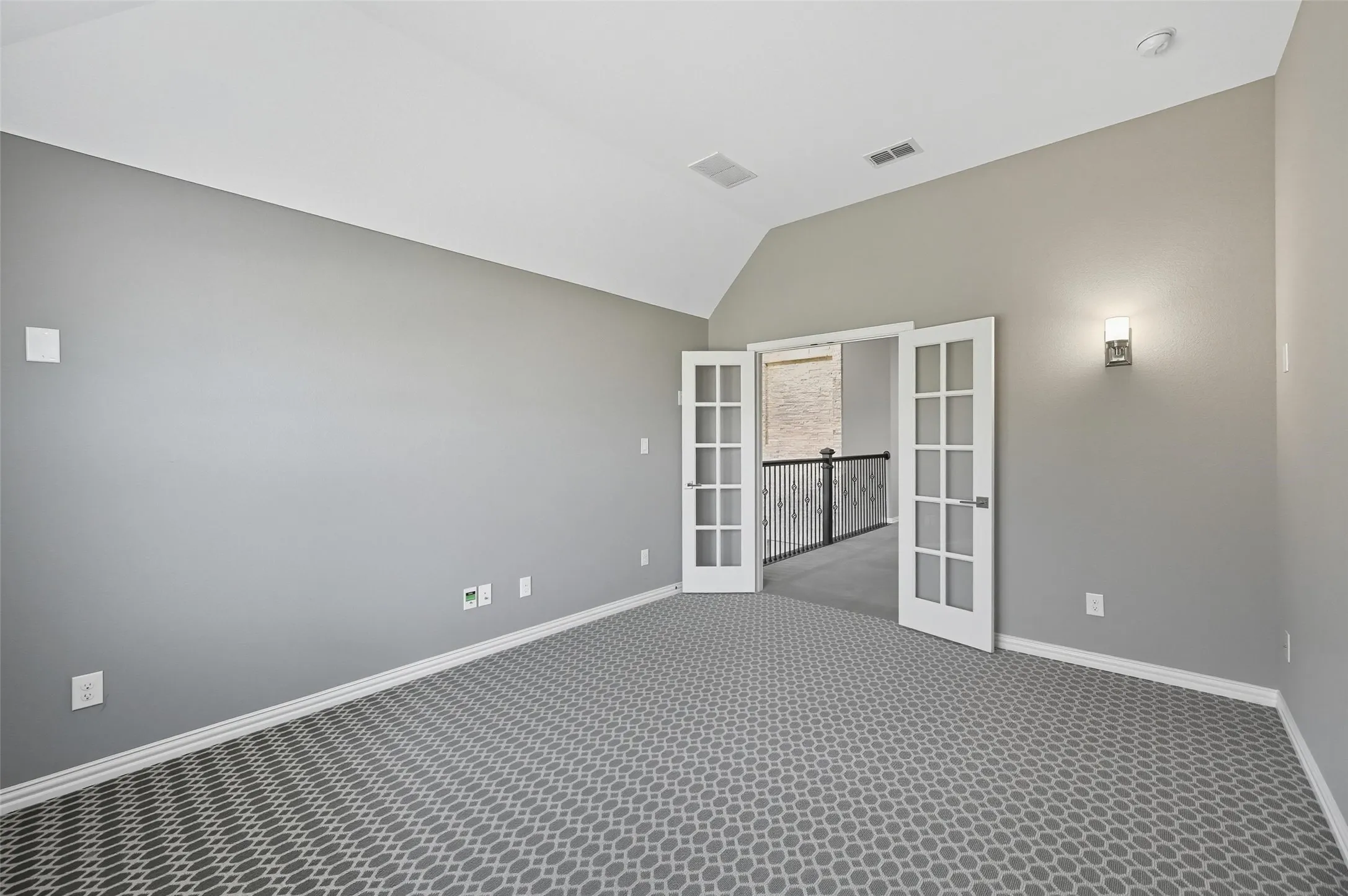 Spacious room featuring vaulted ceilings, patterned carpet flooring, and a wall-mounted sconce
