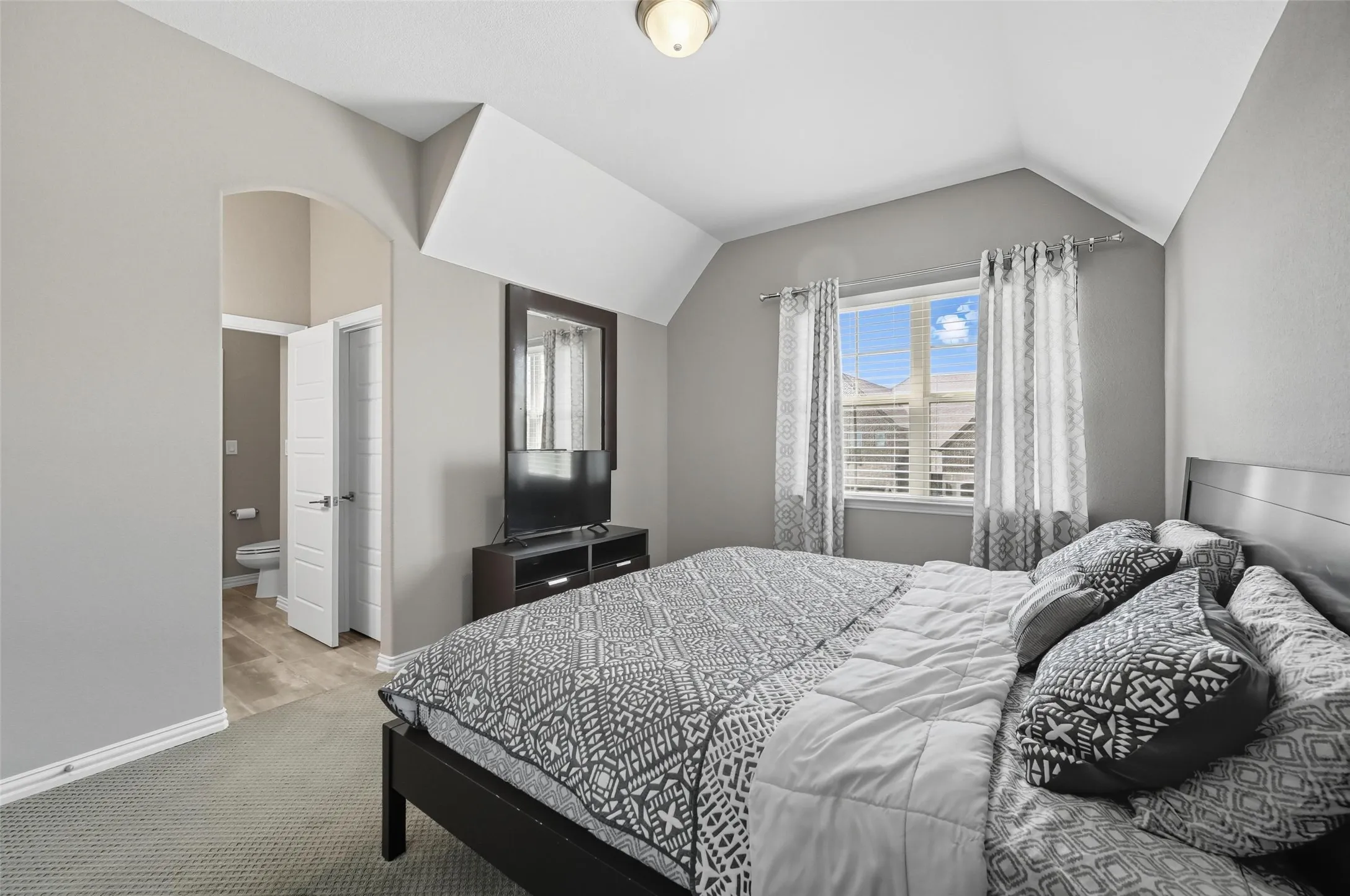 Bedroom featuring an arched doorway, window with blinds, and sloped ceiling