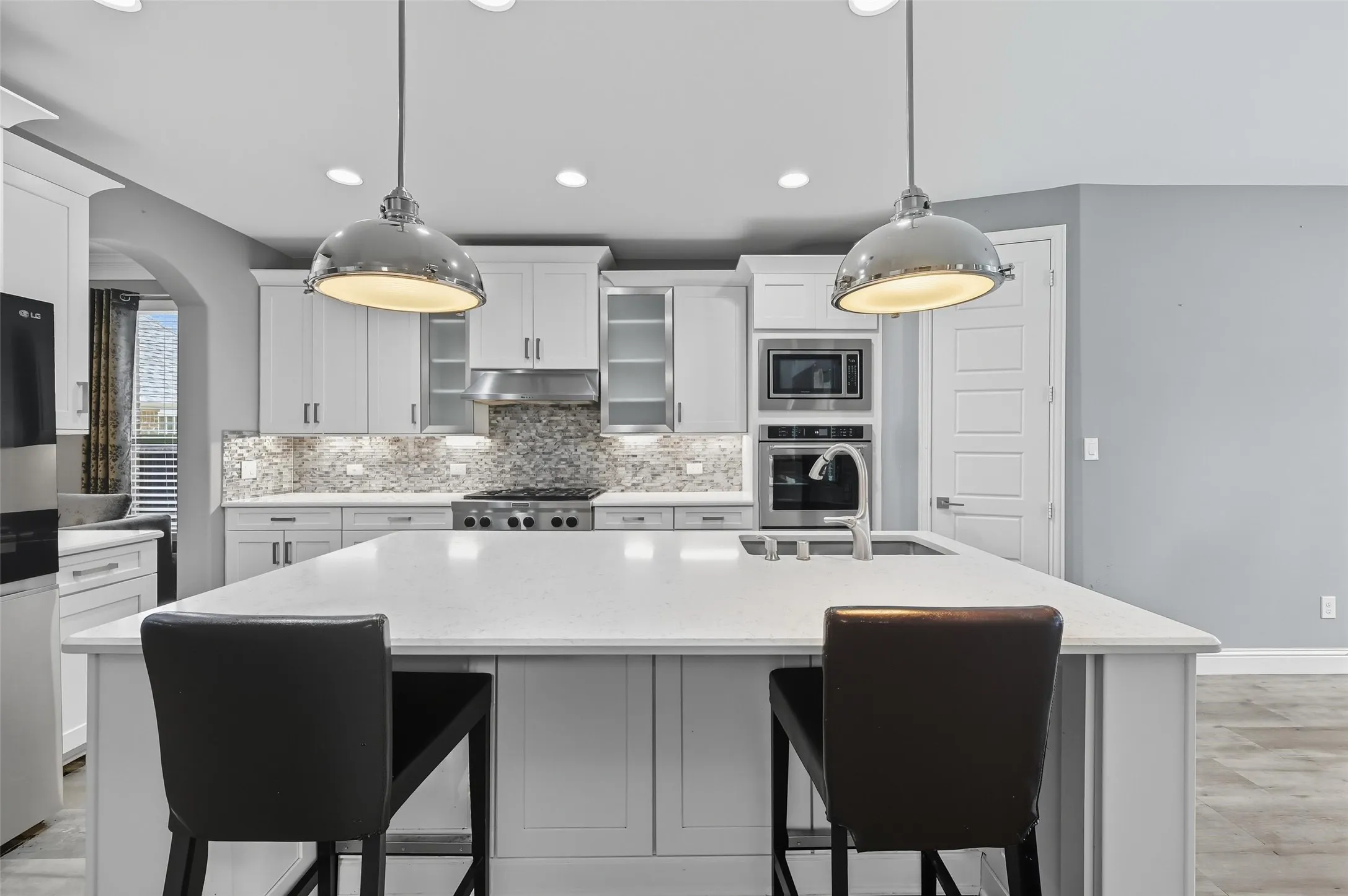 Modern kitchen featuring a large central island with countertop seating, white shaker cabinetry, stainless steel appliances, a mosaic tile backsplash, and recessed lighting